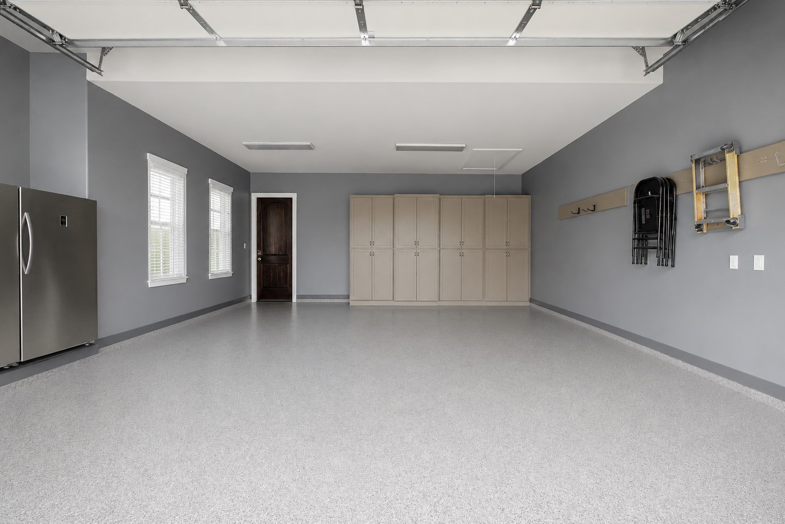 Oversized garage featuring durable epoxy flooring, abundant natural light from multiple windows, and built-in cabinetry for exceptional storage and organization.