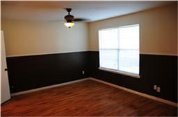 This room features hardwood flooring, a ceiling fan, and a large window. The walls are two-toned with a darker shade on the lower half, creating a stylish contrast.
