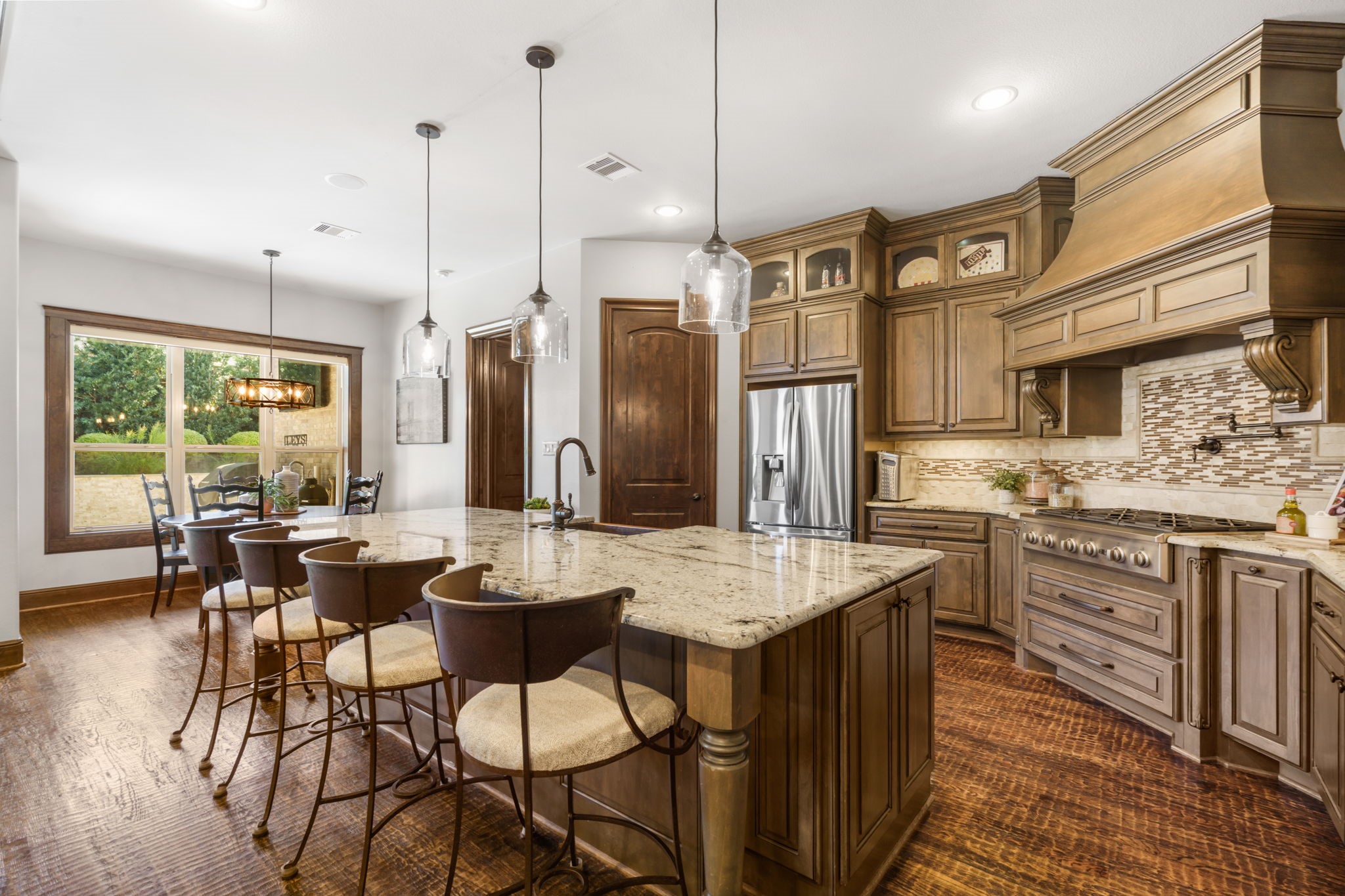 Beautifully appointed kitchen featuring Benedettini custom cabinetry, granite countertops, an oversized island with breakfast bar seating, and elegant pendant lighting.