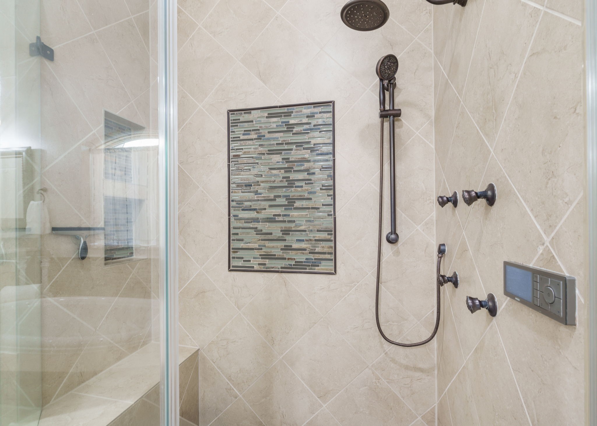 Beautifully tiled shower featuring multiple body sprays, a rainfall showerhead, handheld shower, and decorative mosaic accents.