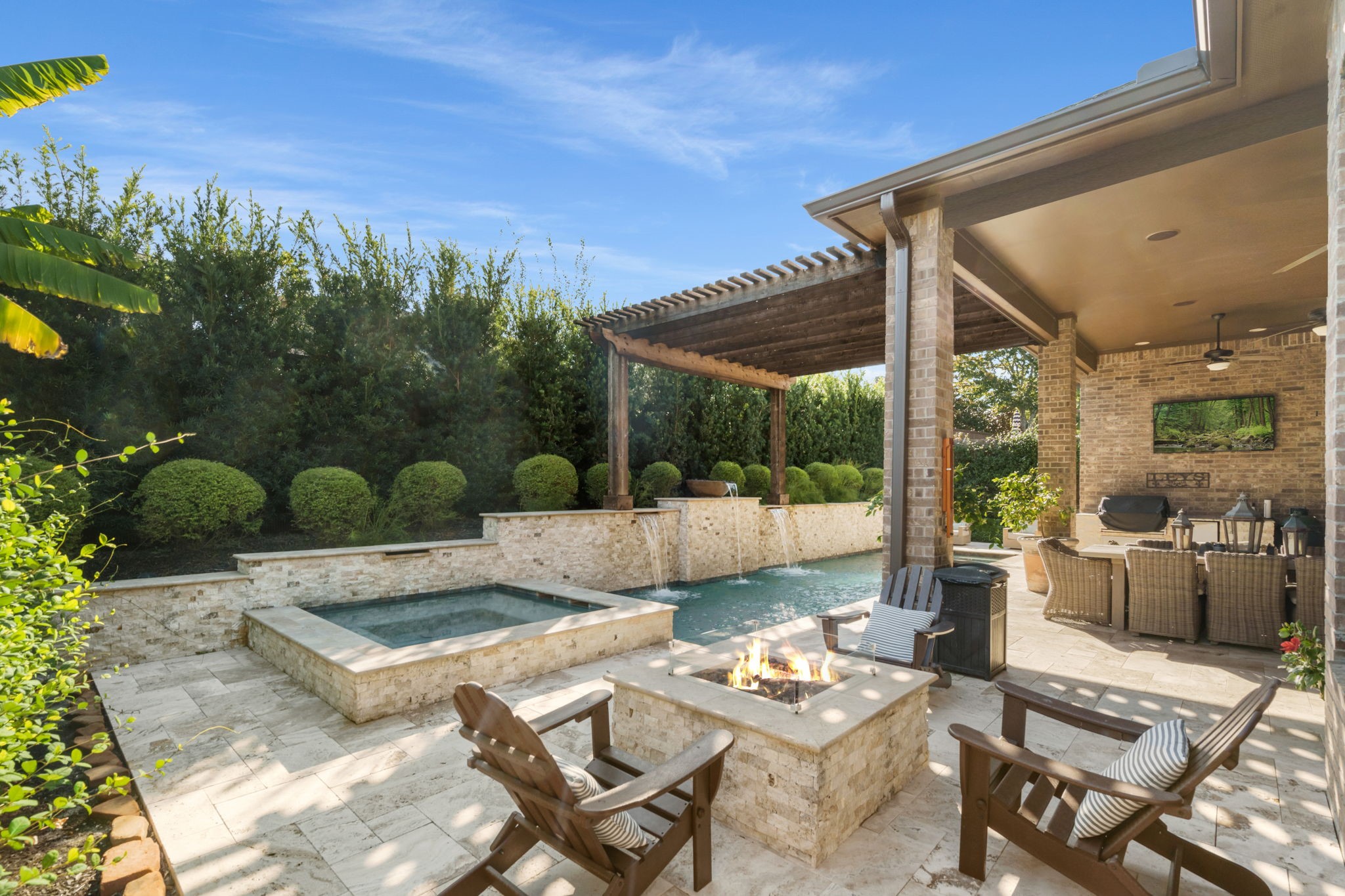 Resort-style backyard featuring a sparkling pool, raised spa, inviting fire-pit, and custom water features.