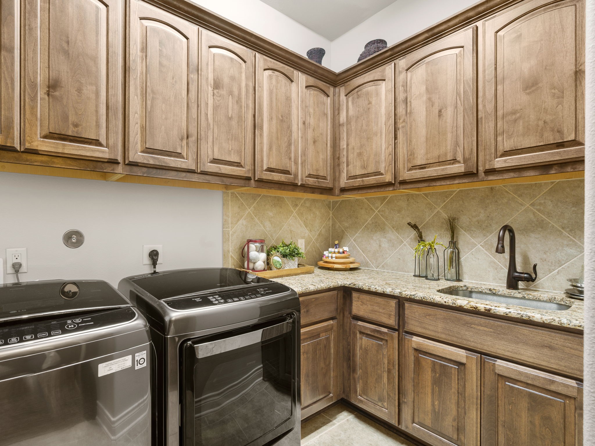 Spacious utility room with abundant upper and lower cabinetry, granite countertops, utility sink, and tile flooring.