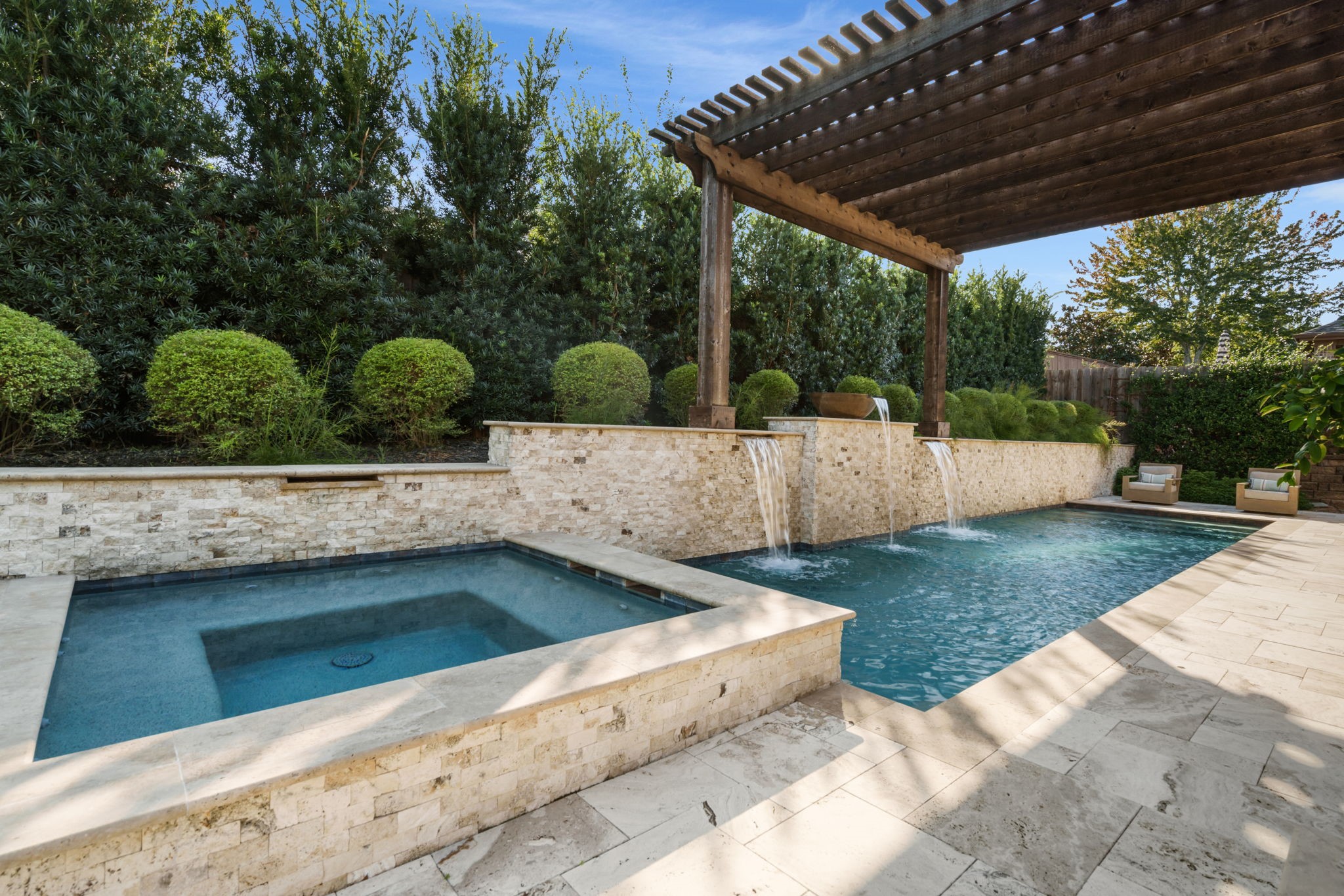 Custom pool showcases cascading waterfalls, a raised stone accent wall, and a beautiful pergola overlooking the water.