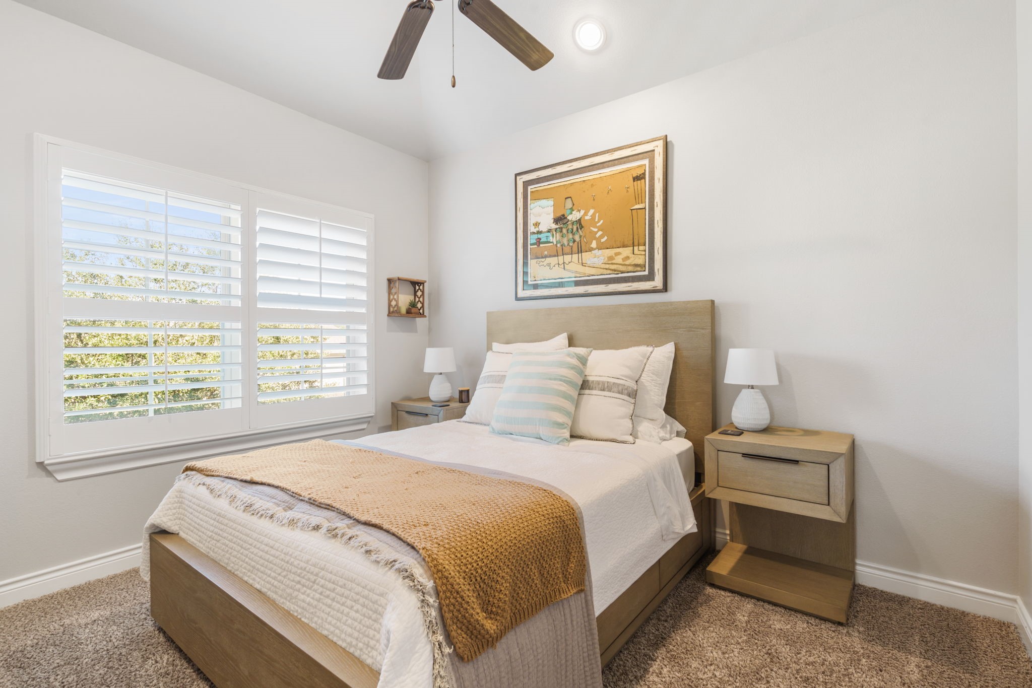 Bright and inviting secondary bedroom with generous natural light, plantation shutters, and a ceiling fan.