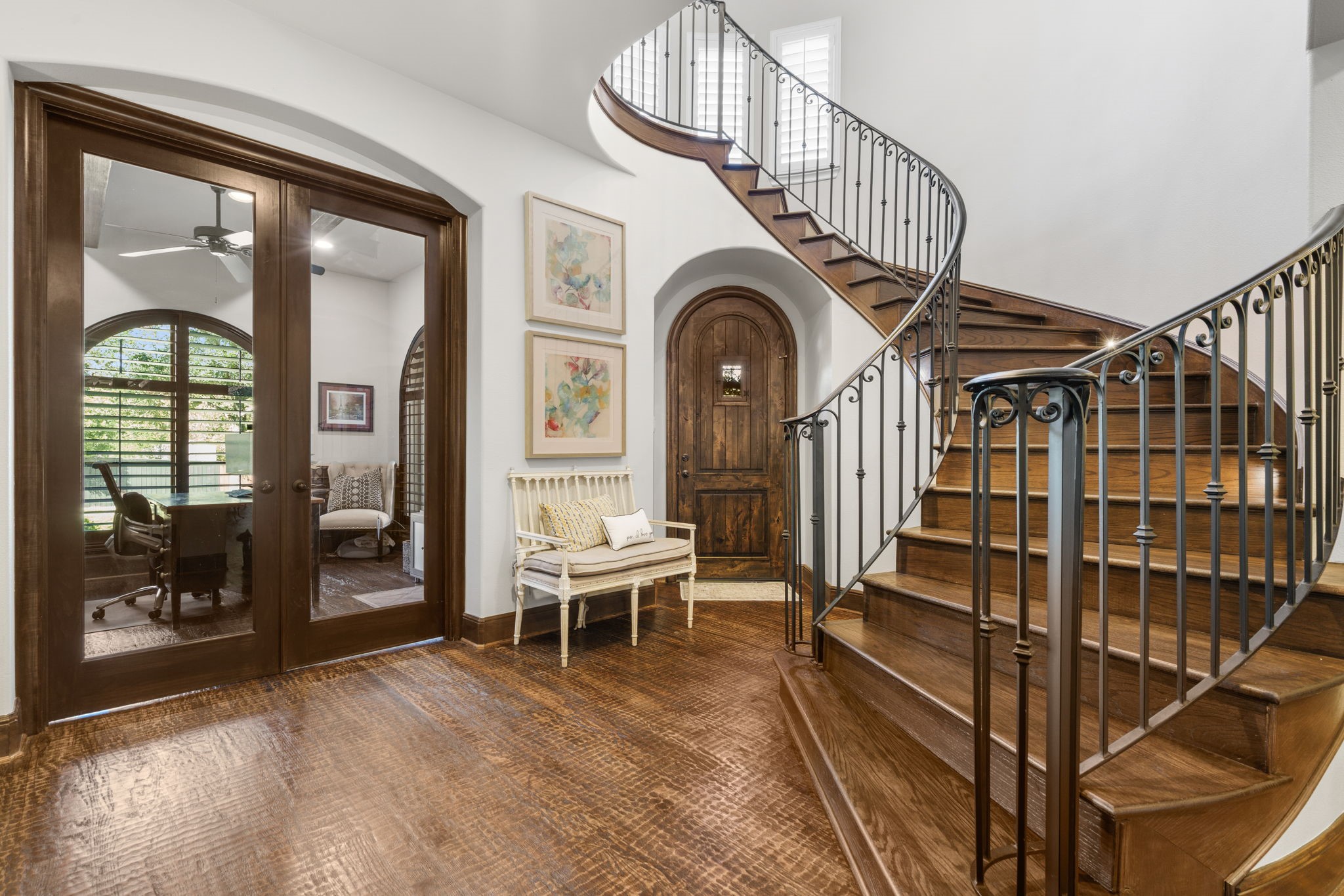 Grand entry featuring an elegant curved staircase with wrought-iron railing, beautiful hand-scraped oak floors, and graceful arched doorways.