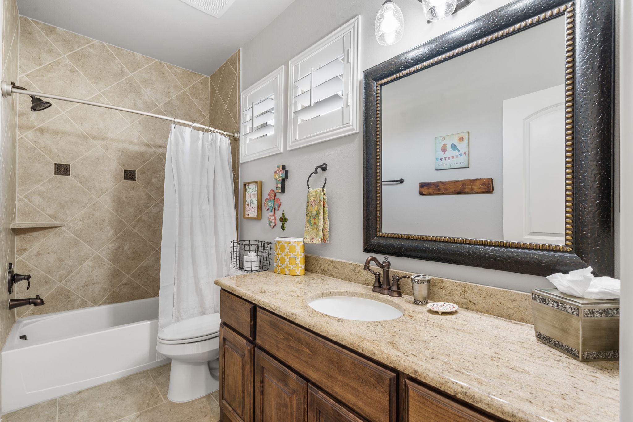 Well-appointed full bathroom featuring granite countertops, rich wood cabinetry, a tub/shower combination, and plantation shutters.