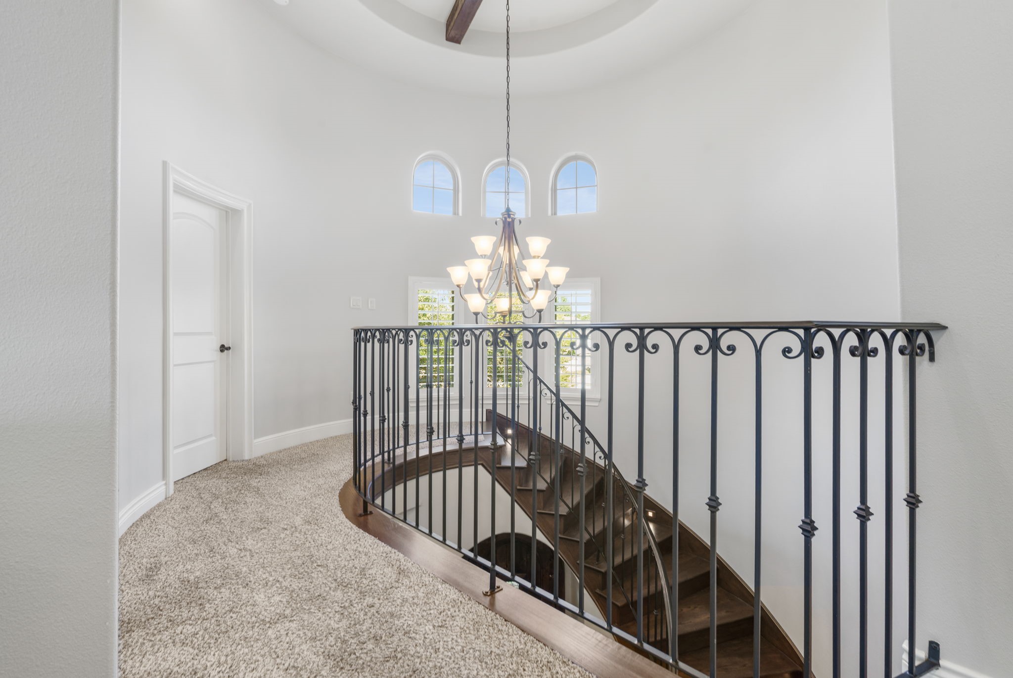 Beautiful curved staircase opens to a bright second-floor landing featuring elegant wrought-iron railings, arched windows, and a statement chandelier.