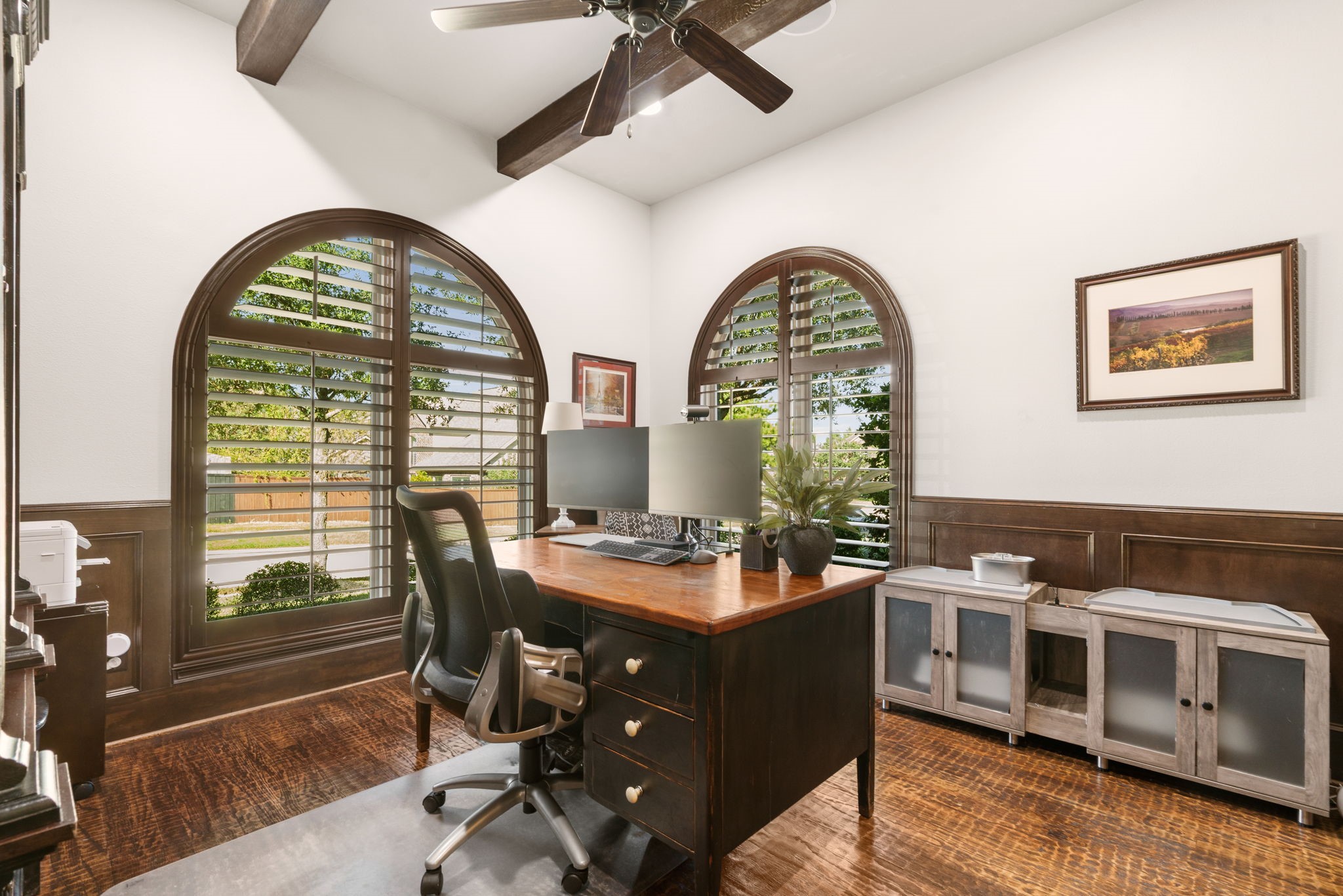 Private home office featuring stunning arched windows with plantation shutters, exposed ceiling beams, and abundant natural light.
