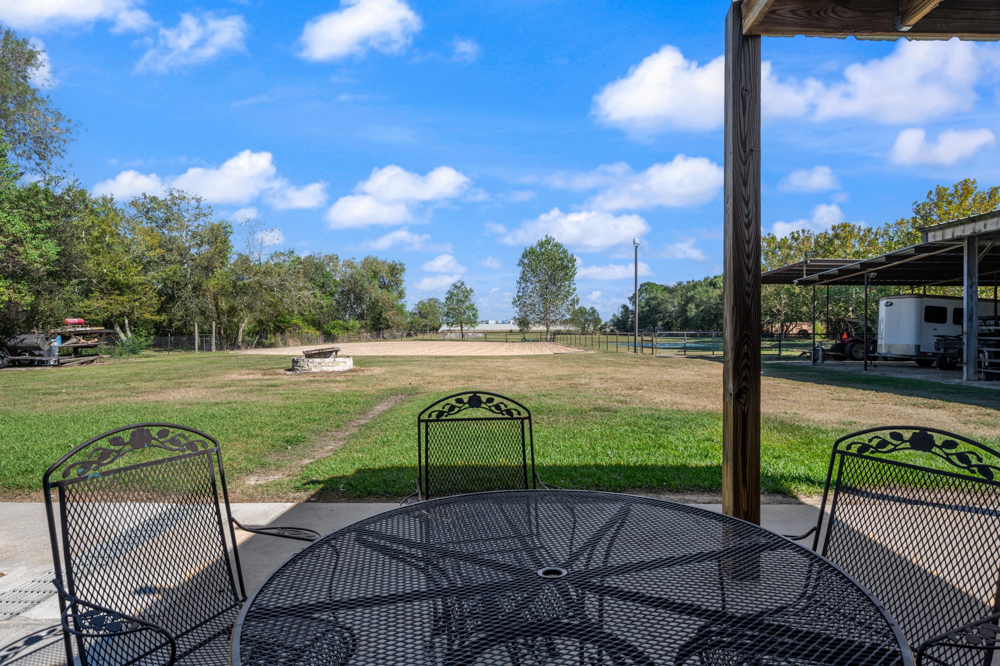 Enjoy peaceful views of the property's equestrian amenities from this covered outdoor seating area. Overlooking the fenced riding arena, open green space, and covered equipment and trailer parking, this inviting spot offers the perfect place to relax while taking in the beauty of country living.