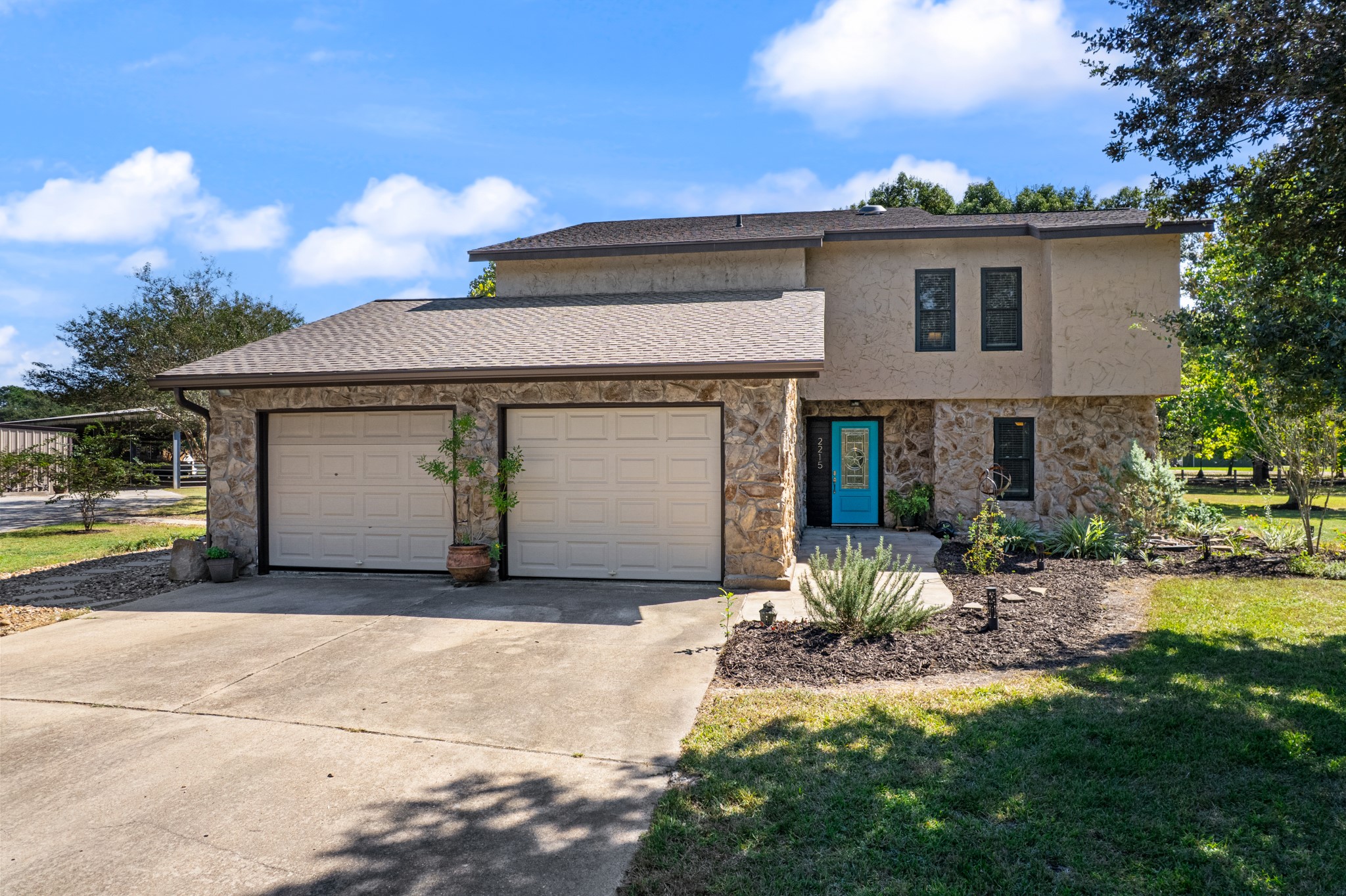 Welcoming exterior view of this distinctive two-story home, featuring a beautiful combination of natural stone and stucco, an attached two-car garage, and a charming turquoise front door. Mature shade trees, landscaped garden beds, and a spacious concrete driveway enhance the home's curb appeal, creating an inviting entrance to this unique country property. Welcoming exterior view of this distinctive two-story home, featuring a beautiful combination of natural stone and stucco, an attached two-car garage, and a charming turquoise front door. Mature shade trees, landscaped garden beds, and a spacious concrete driveway enhance the home's curb appeal, creating an inviting entrance to this unique country property.