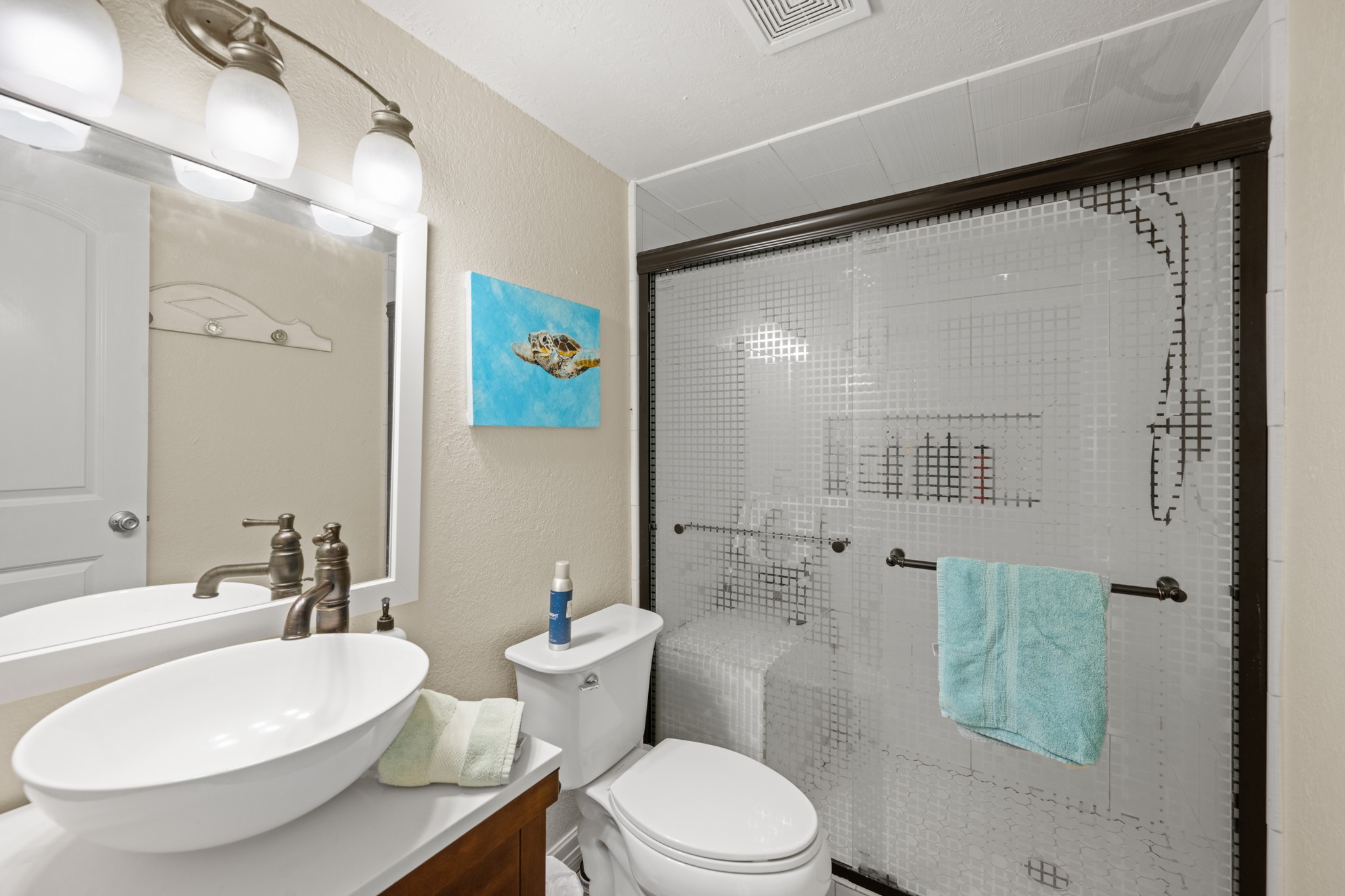 Stylish bathroom features a contemporary vessel sink, brushed-nickel fixtures, and a tub/shower combination with decorative glass sliding doors and tile surround.