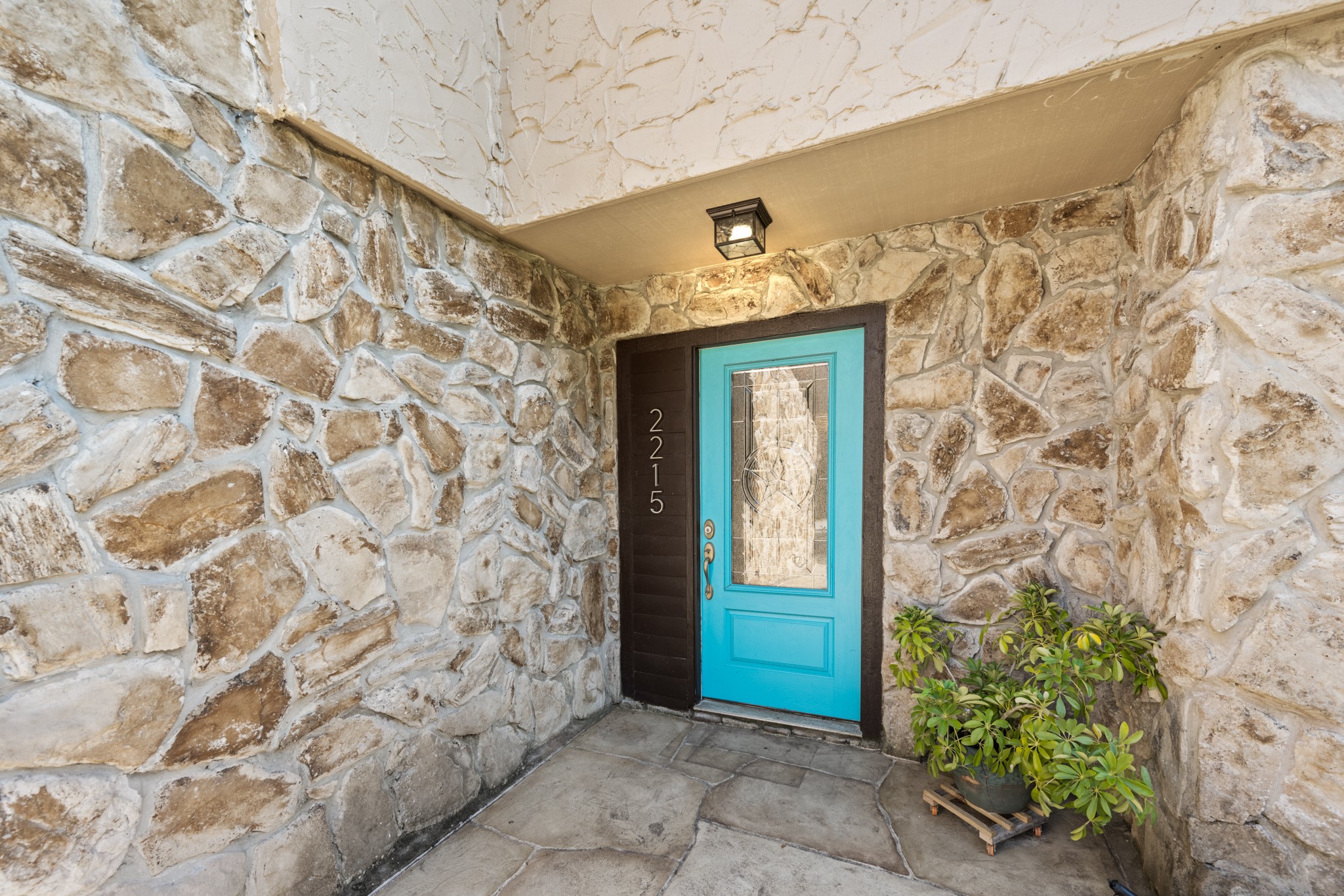A welcoming covered entry showcases rustic stone walls, stone-look flooring, and a striking turquoise front door with decorative glass, adding a vibrant touch of character to the home's exterior. A welcoming covered entry showcases rustic stone walls, stone-look flooring, and a striking turquoise front door with decorative glass, adding a vibrant touch of character to the home's exterior.