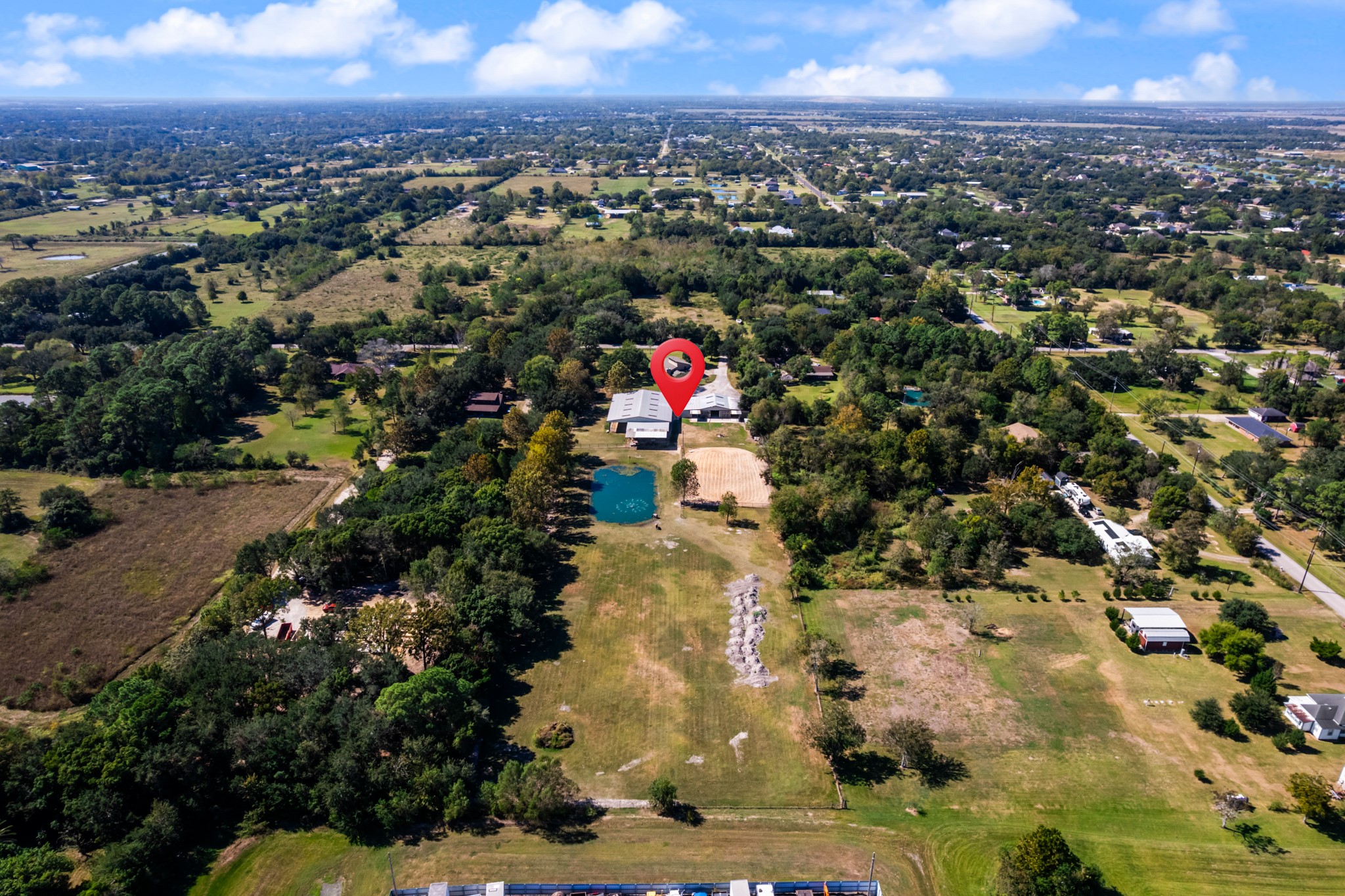A birds-eye view showcases the property's expansive grounds, featuring open pastureland, a picturesque pond, mature trees, and equestrian facilities. A beautiful blend of open space and natural surroundings offers plenty of room for horses, outdoor recreation, and enjoying the peaceful country setting while remaining close to nearby conveniences.