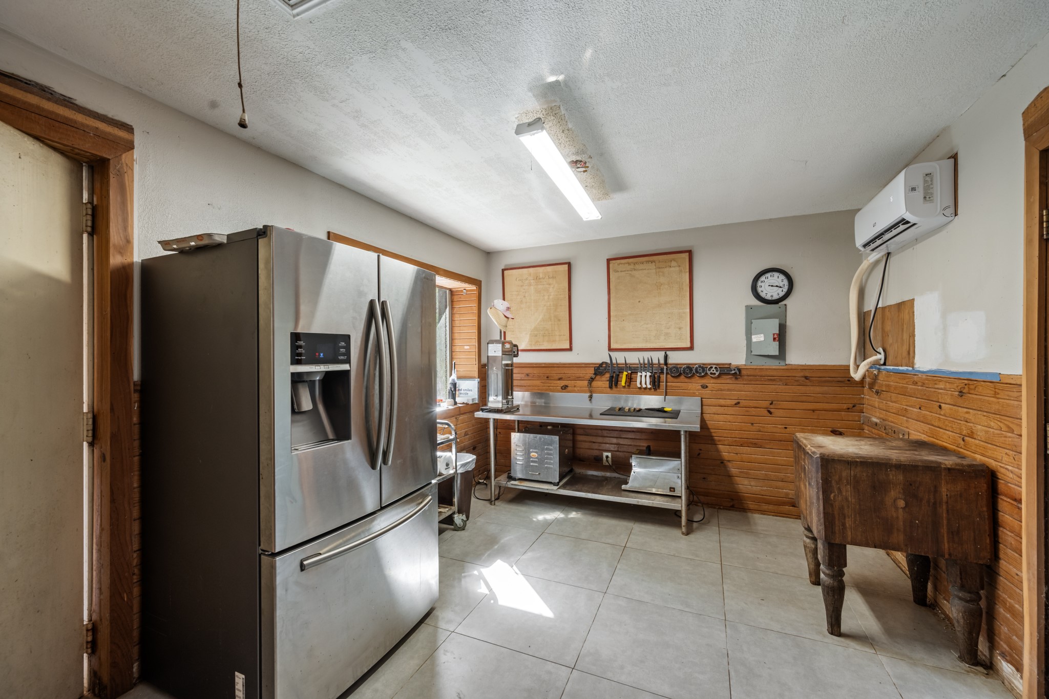 Dedicated food preparation and utility space with stainless steel workstations, full-size refrigerator, butcher block table, tiled flooring, and wall-mounted mini-split system.