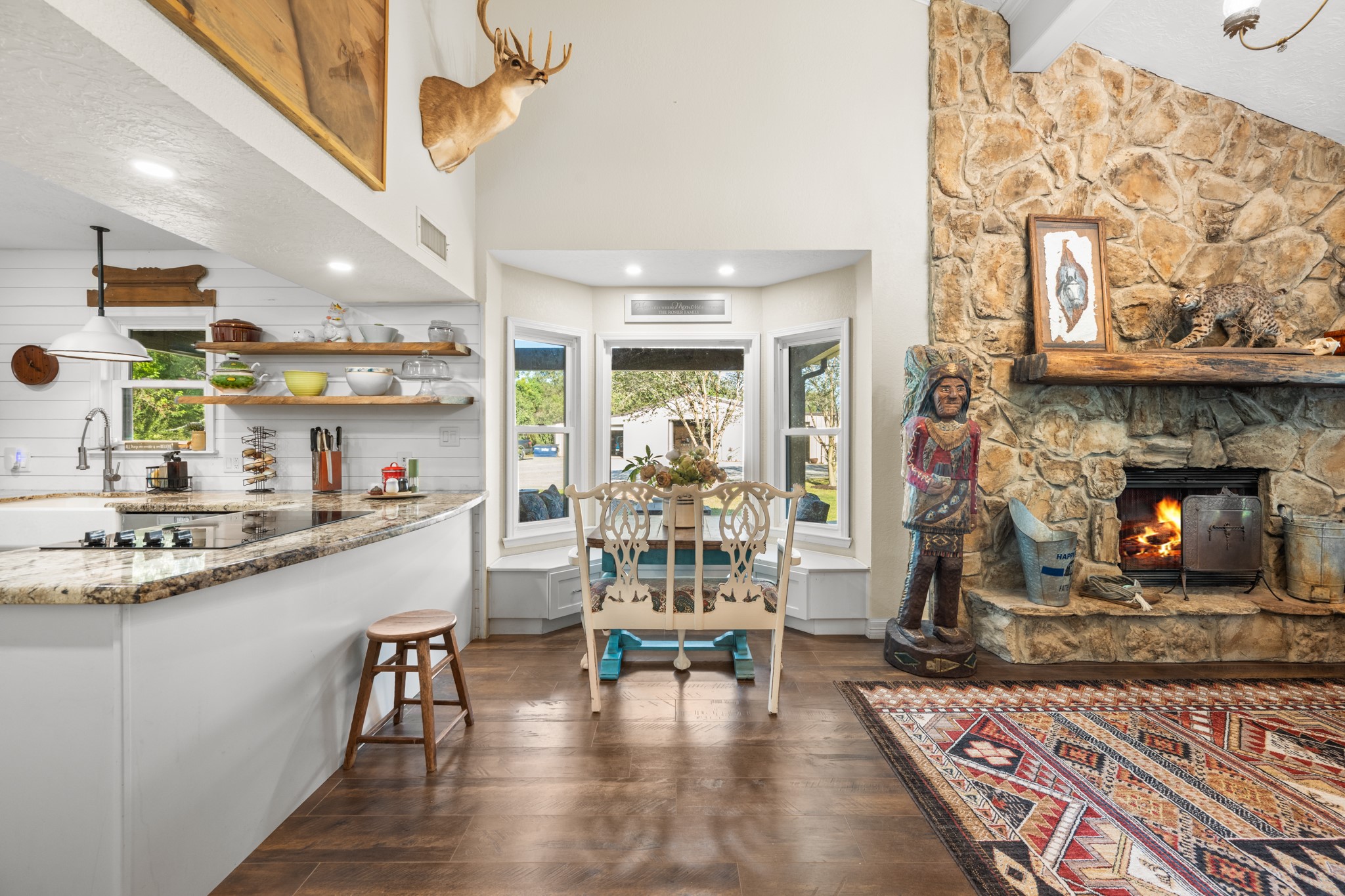 A charming window-lined breakfast nook with built-in seating connects the farmhouse kitchen and living area, where soaring ceilings and a dramatic stone fireplace create an inviting atmosphere.
