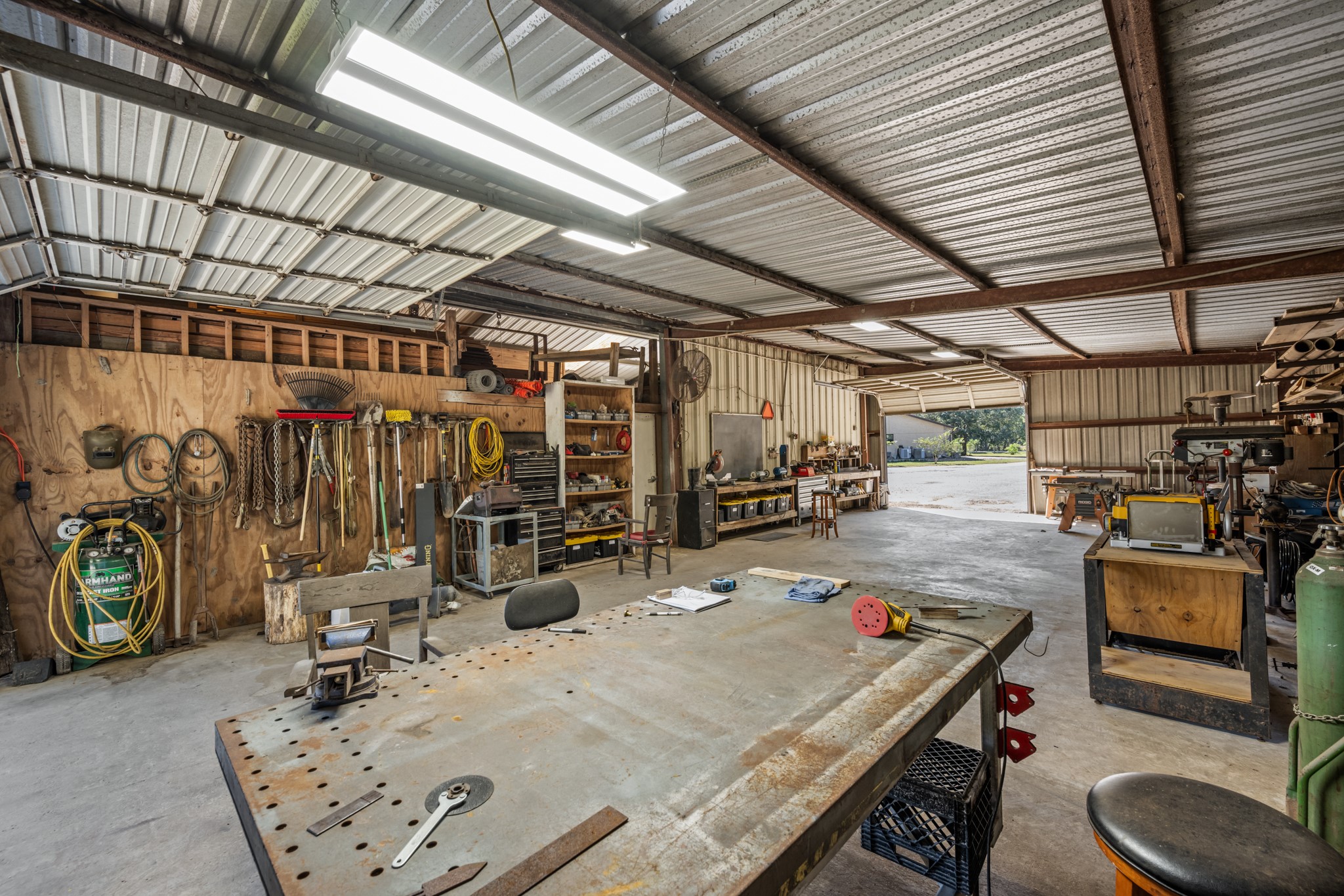 Another view of the impressive workshop, showcasing a large central worktable, extensive tool storage, built-in workstations, and convenient overhead roll-up door access.