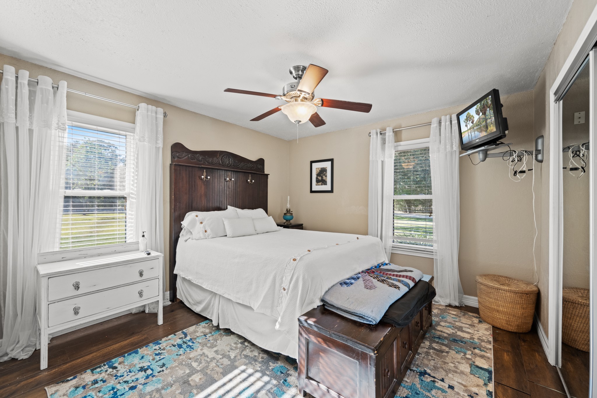 Inviting downstairs guest bedroom offers two windows overlooking the property, warm wood-look flooring, a ceiling fan, and a mirrored closet.