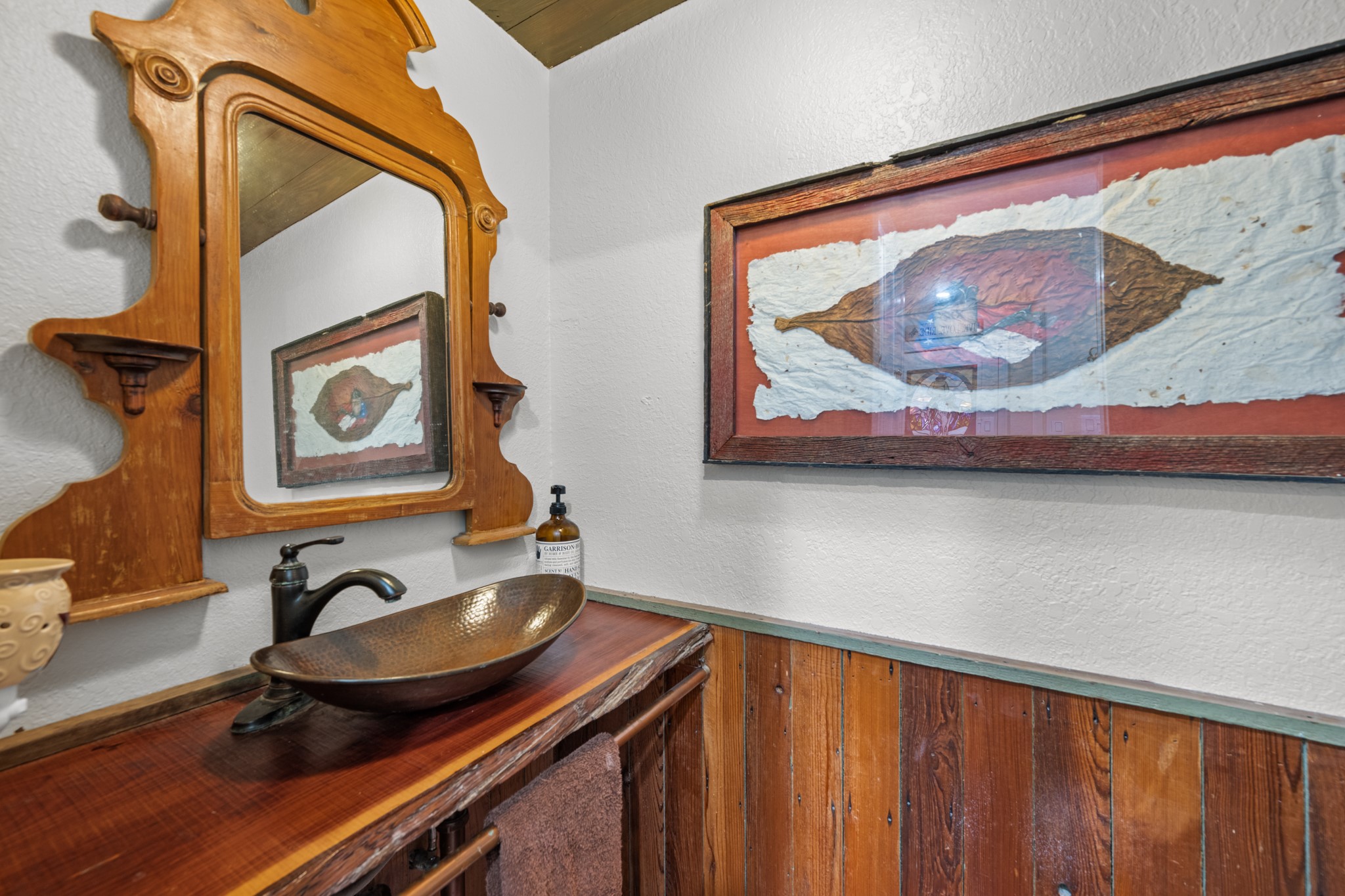 Full of rustic character, this charming half bath features a distinctive hammered-metal vessel sink, rich wood countertop, vintage-style framed mirror, and warm wood wainscoting.