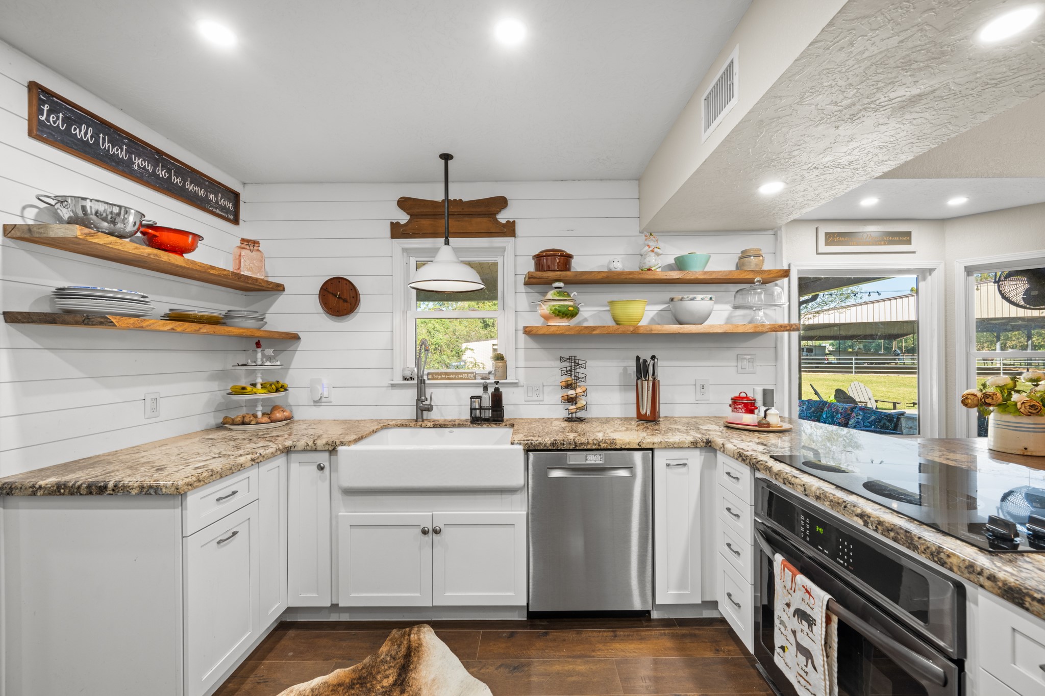 A beautiful apron-front farmhouse sink, gooseneck faucet, granite countertops, and floating wood shelves combine style with everyday functionality.
