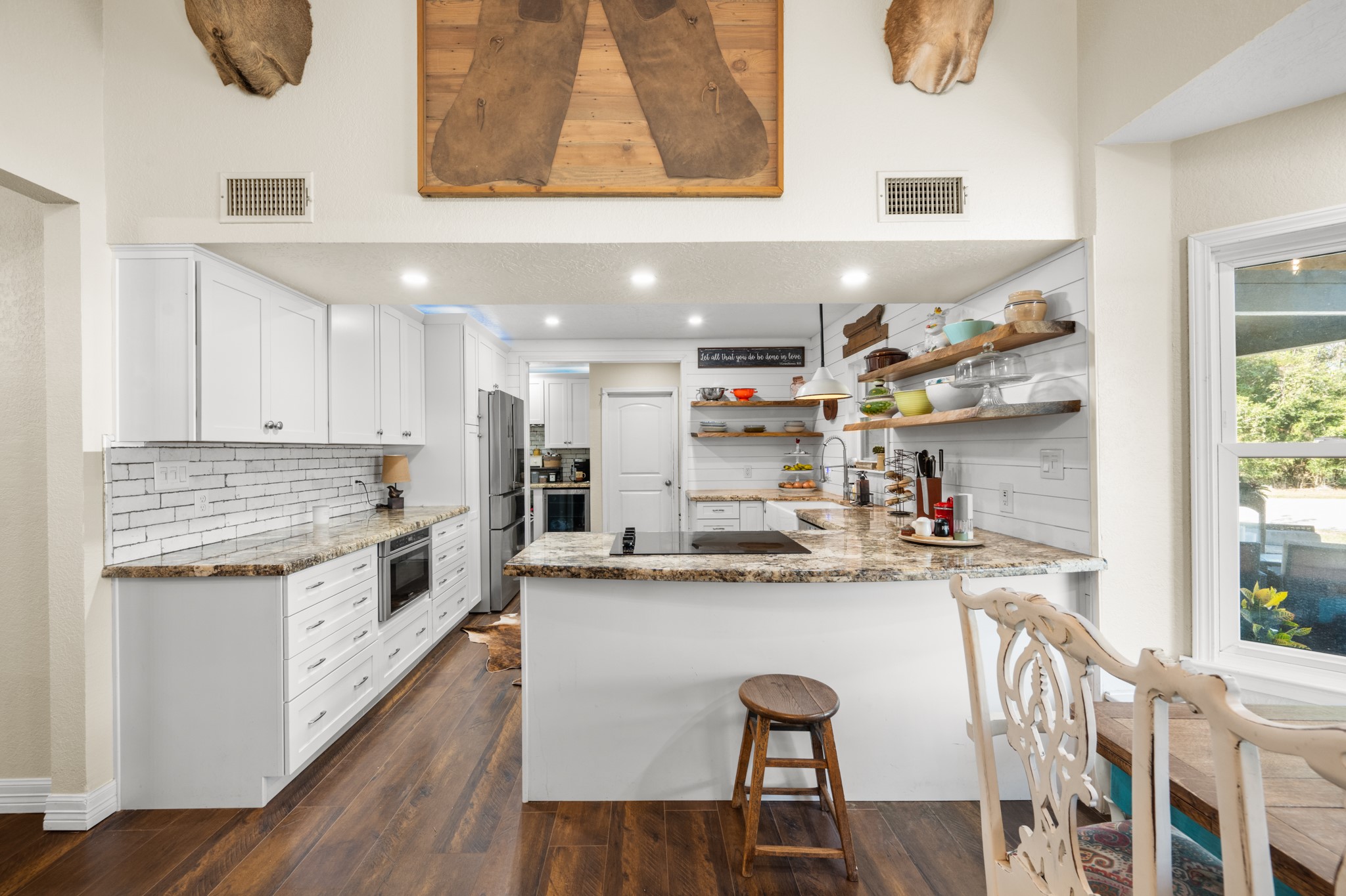 Farmhouse charm meets modern convenience with granite countertops, crisp white cabinetry, floating wood shelves, and a generous breakfast bar with an electric cooktop.