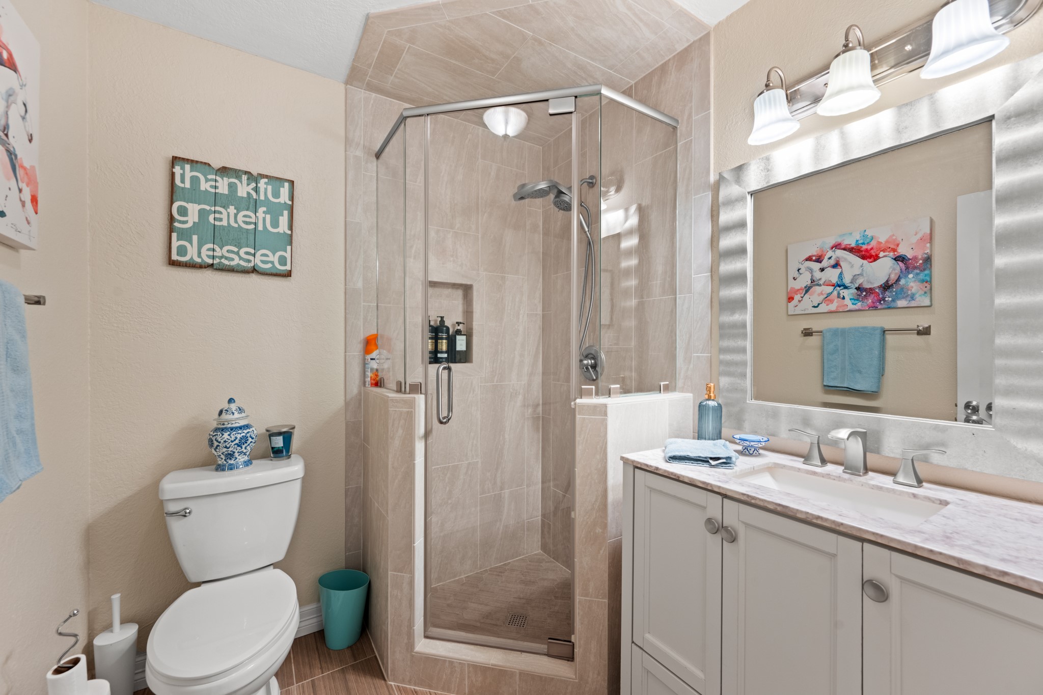 Beautifully appointed bathroom features a glass-enclosed tiled shower with built-in niche, a spacious vanity, brushed-nickel fixtures, and contemporary finishes.