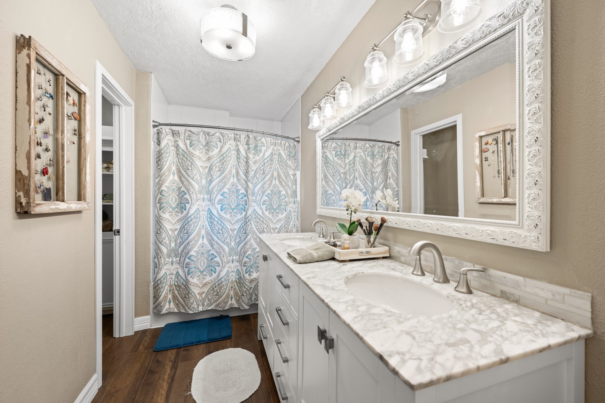 The primary bathroom offers a generous double-sink vanity with stone-look countertops, decorative tile backsplash, oversized framed mirror, and a tub/shower combination with access to a walk-in closet.