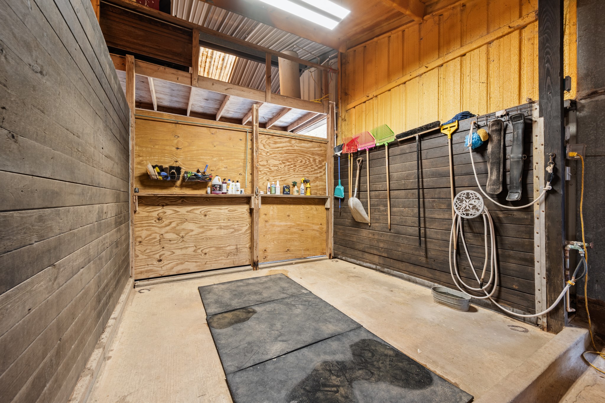Dedicated horse wash and grooming bay featuring rubber floor mats, wood-paneled walls, water access, and convenient storage for grooming essentials.