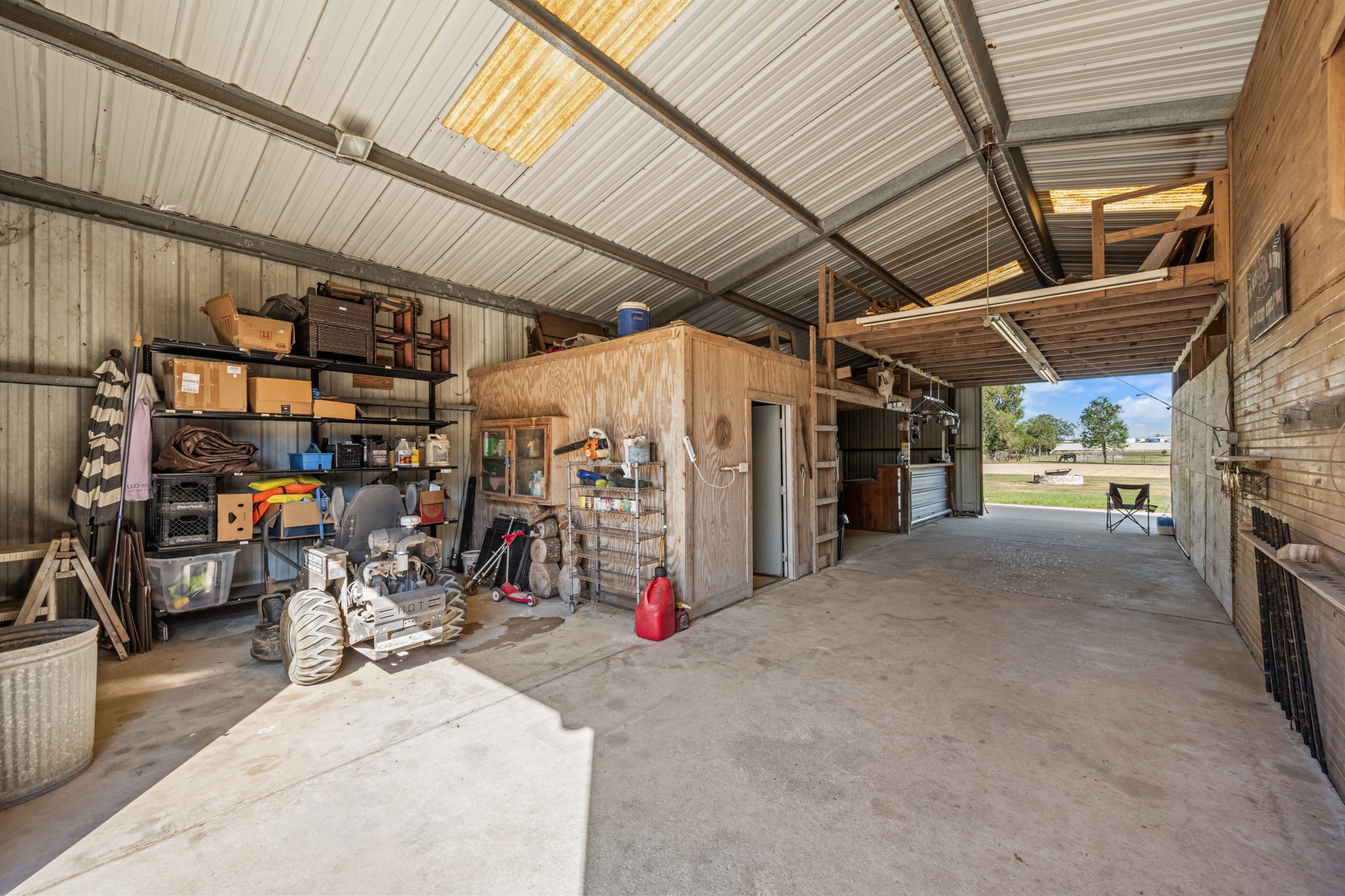 Versatile covered workspace featuring concrete floors, built-in shelving, enclosed storage, overhead loft space, and easy access to the surrounding property.