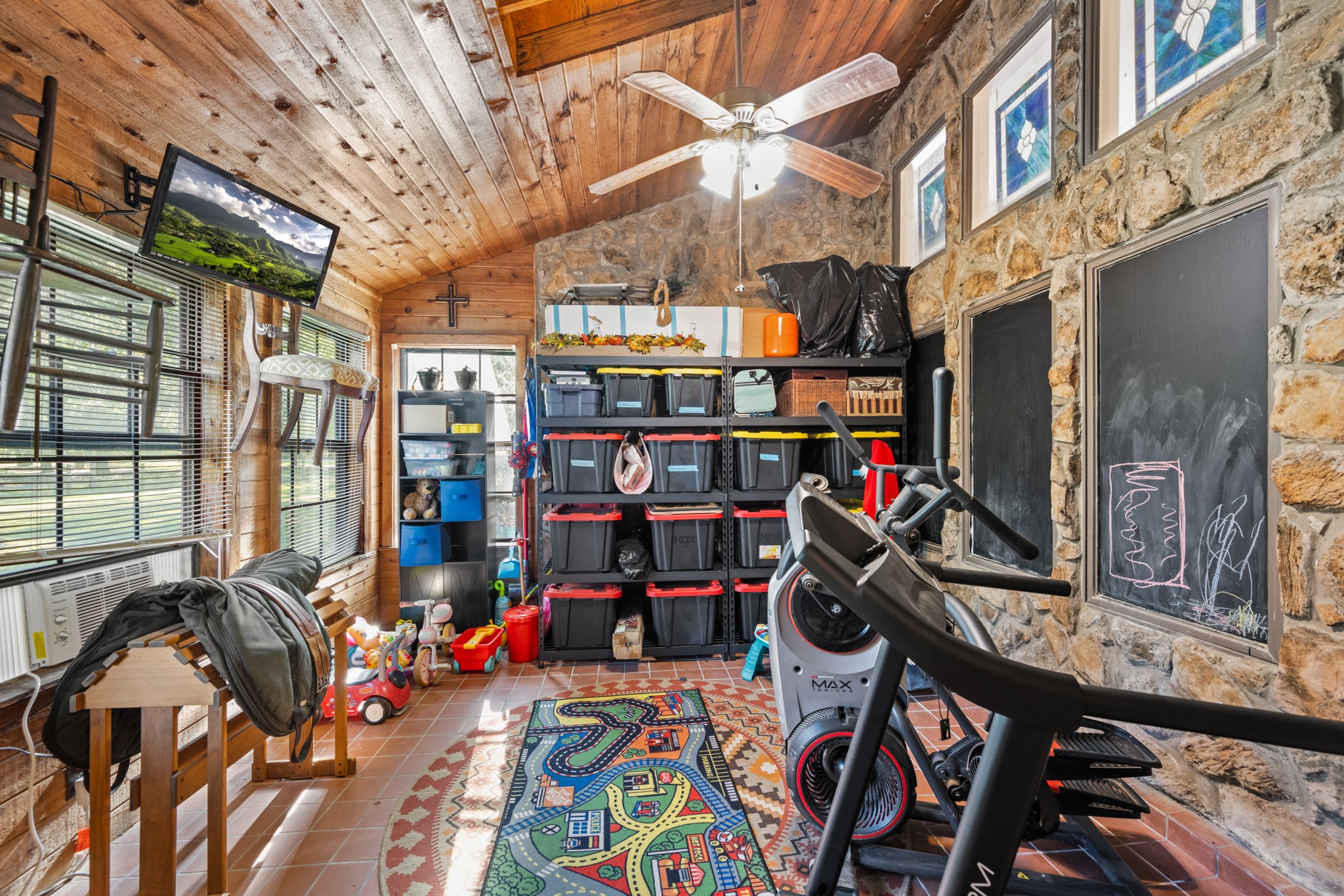 Versatile bonus space showcases a vaulted wood-plank ceiling, exposed stone walls, abundant windows, and tile flooring. Ideal for a home gym, hobby room, playroom, or additional flex space.