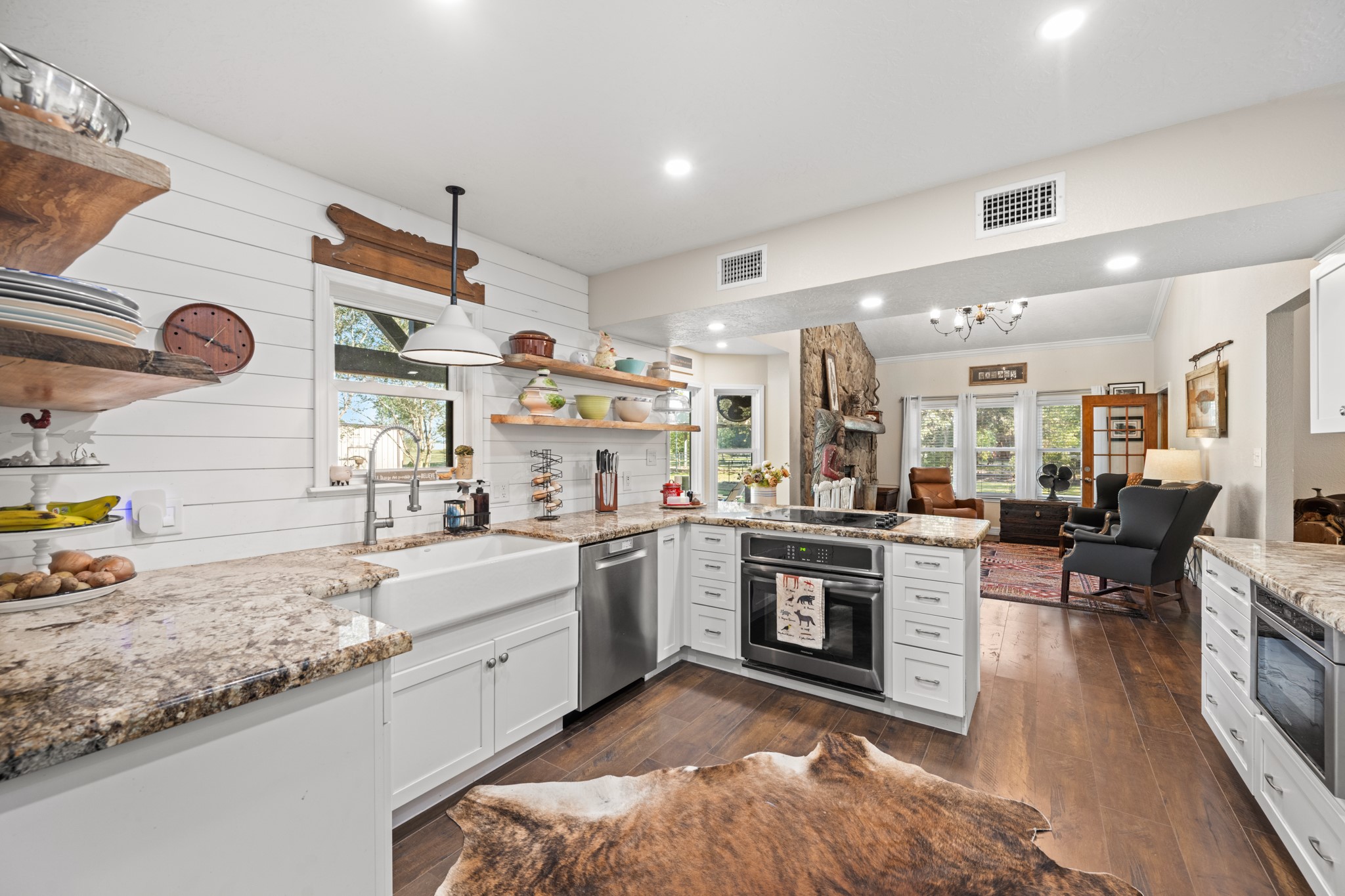 Rustic farmhouse details take center stage with white shiplap walls, natural wood shelving, a farmhouse sink, and warm wood-look flooring.