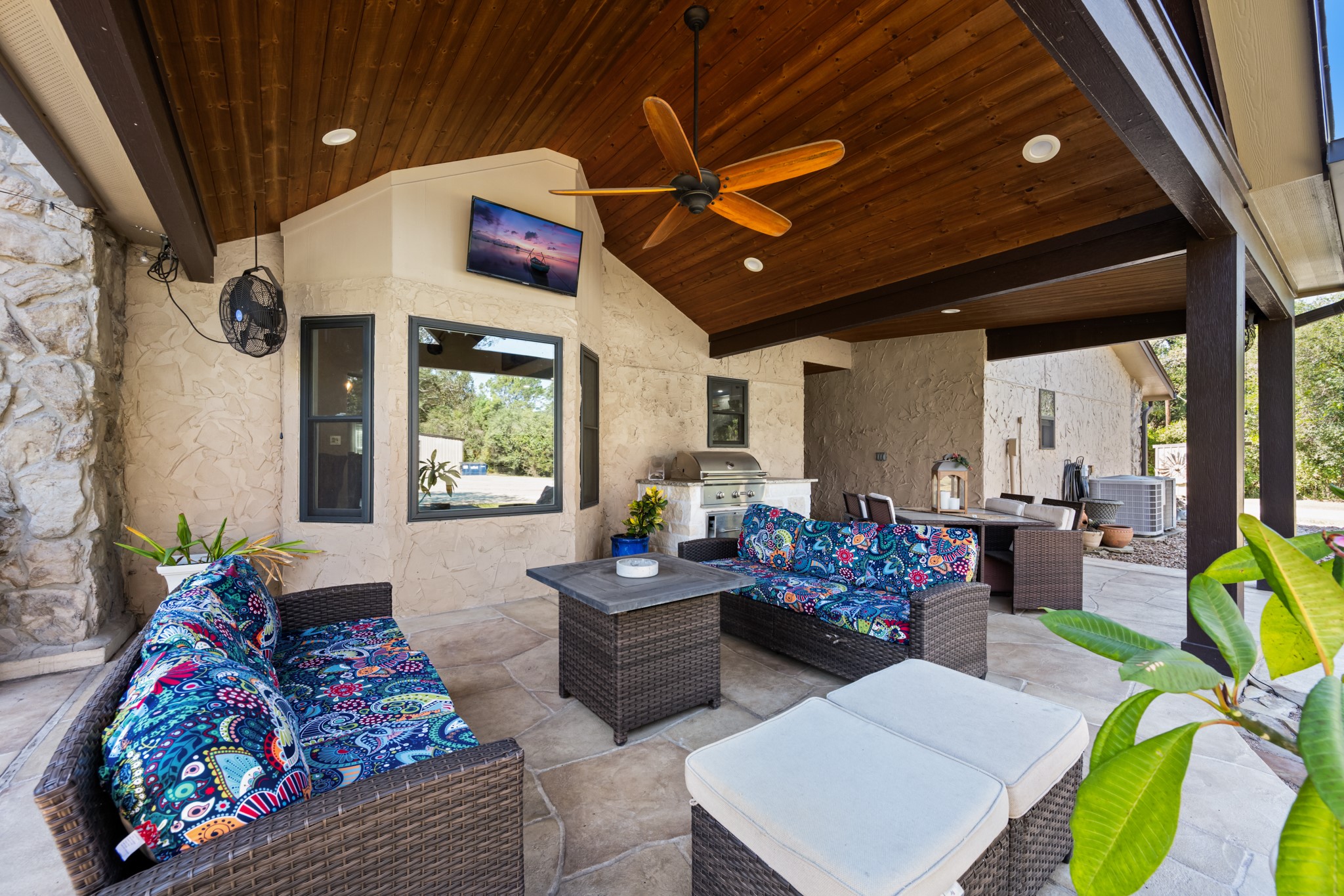 Enjoy outdoor living beneath a spacious covered patio featuring a beautiful wood-plank ceiling, exposed beams, ceiling fan, comfortable seating area, and built-in grilling station. An inviting extension of the home, perfect for relaxing or entertaining.