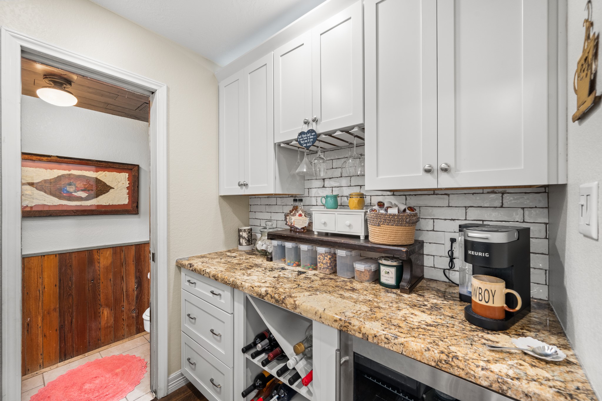 A dedicated coffee and beverage station/butlers pantry offers granite countertops, custom-style cabinetry, built-in wine storage, hanging stemware racks, and an undercounter beverage refrigerator.