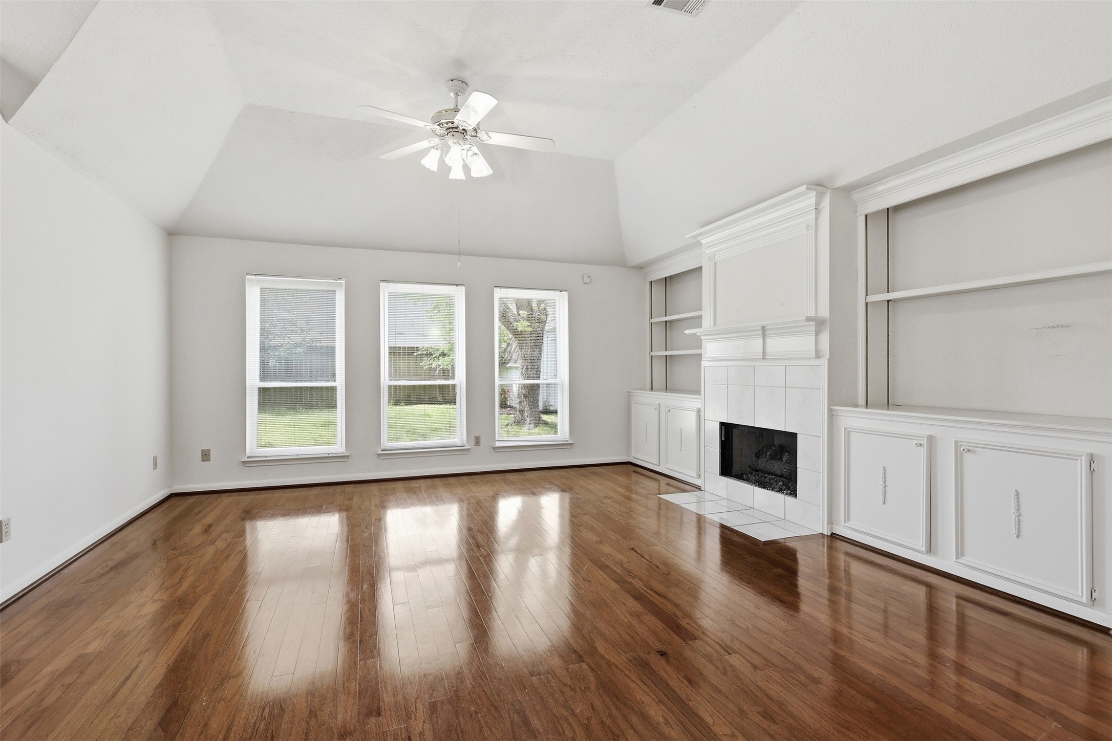 A warm, spacious gathering area featuring polished wood floors, vaulted ceiling, and a classic fireplace with built-ins. A warm, spacious gathering area featuring polished wood floors, vaulted ceiling, and a classic fireplace with built-ins.
