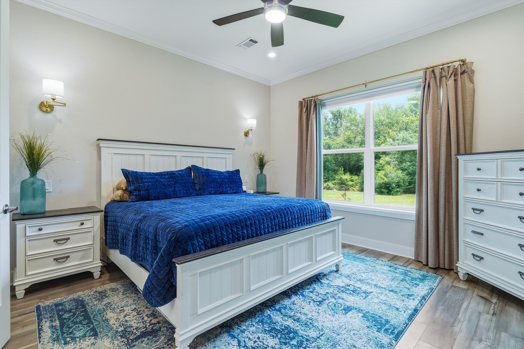 Primary bedroom with sconces, ceiling fan and double window overlooking the property