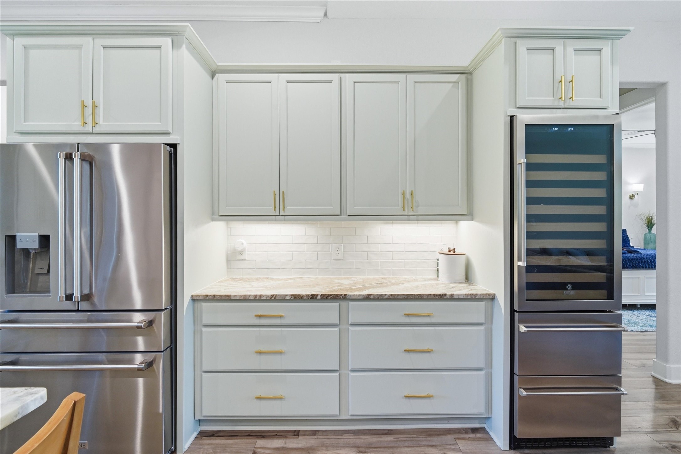 Popular shaker style cabinets with brushed brass hardware, pull out drawers accented by under cabinet lighting. Stainless steel wine refrigerator with beverage bins.