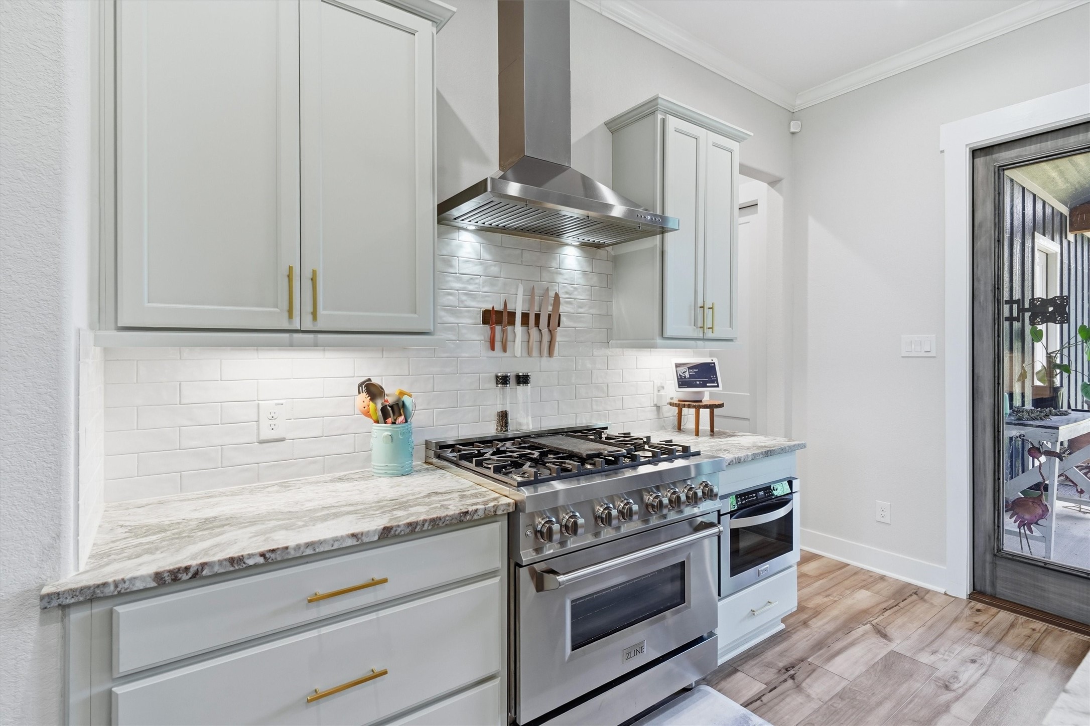 Stainless steel vent hood, gas range and microwave drawer. Shaker style cabinetry, useful set of drawers, brushed brass hardware and under cabinet lighting illuminates workspace.