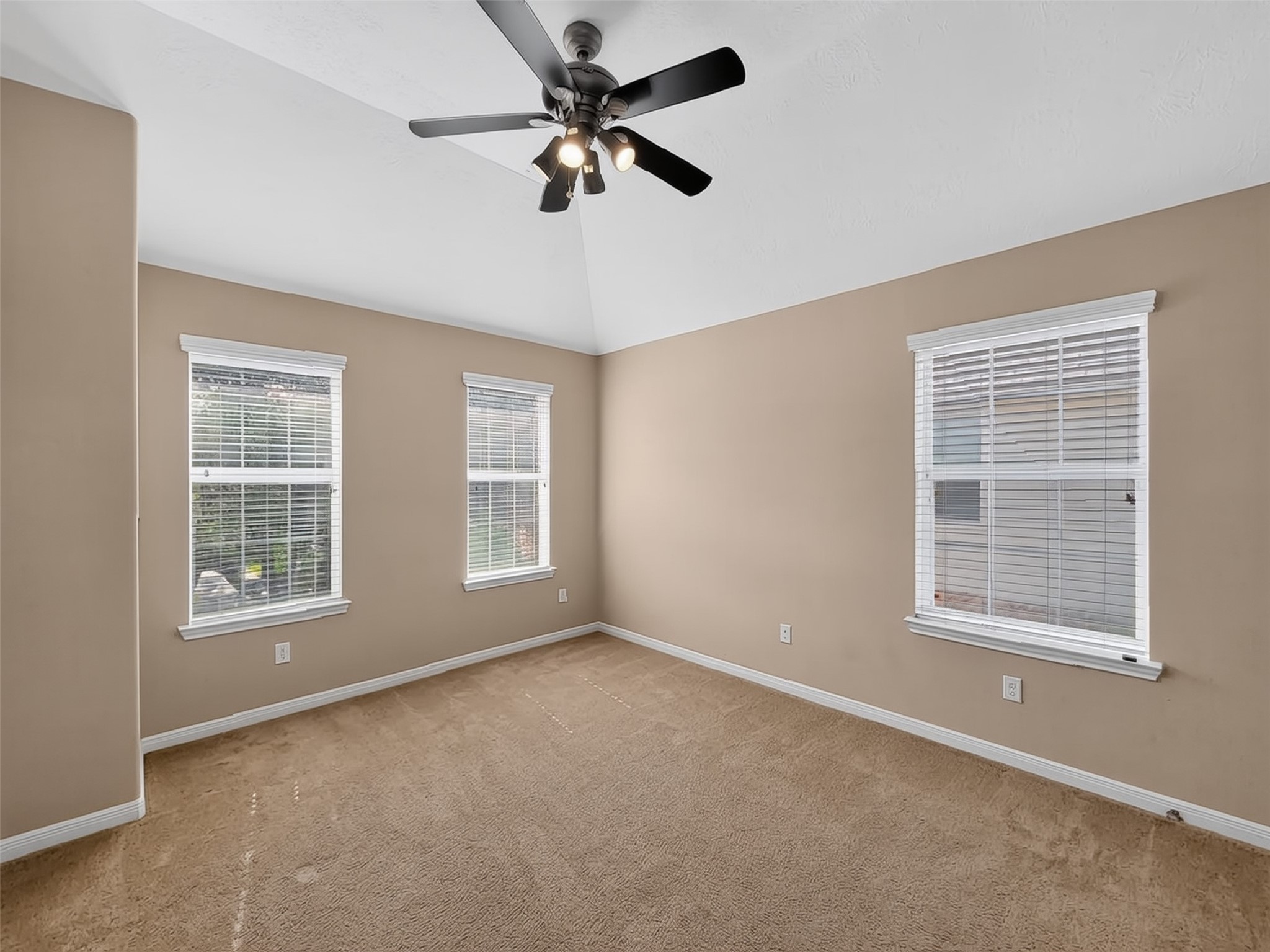 Spacious and bright room with neutral walls, plush carpet, and a ceiling fan, featuring three large windows for ample natural light.