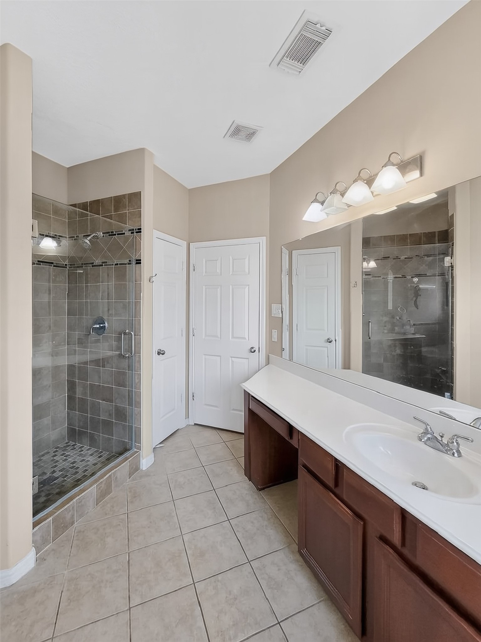 Spacious bathroom featuring a large walk-in shower with sleek glass doors, dual vanity with ample counter space, and elegant tile flooring.