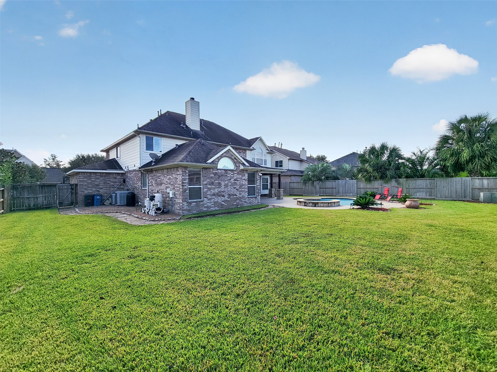Expansive backyard with lush green lawn, featuring a brick exterior, patio area, and inviting pool for outdoor relaxation and entertainment.