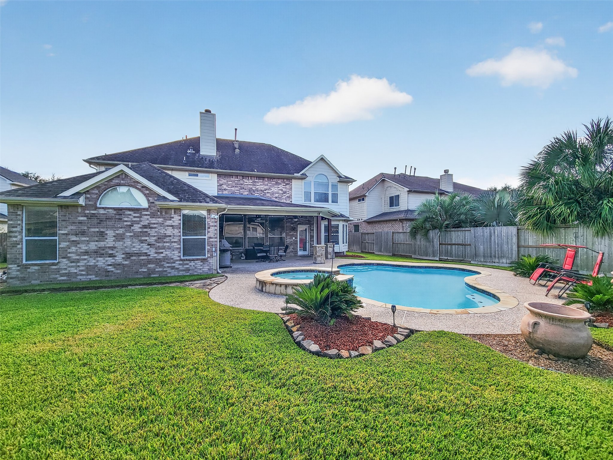 Charming two-story brick home with a spacious backyard featuring a sparkling pool, lush landscaping, and a covered patio perfect for entertaining.