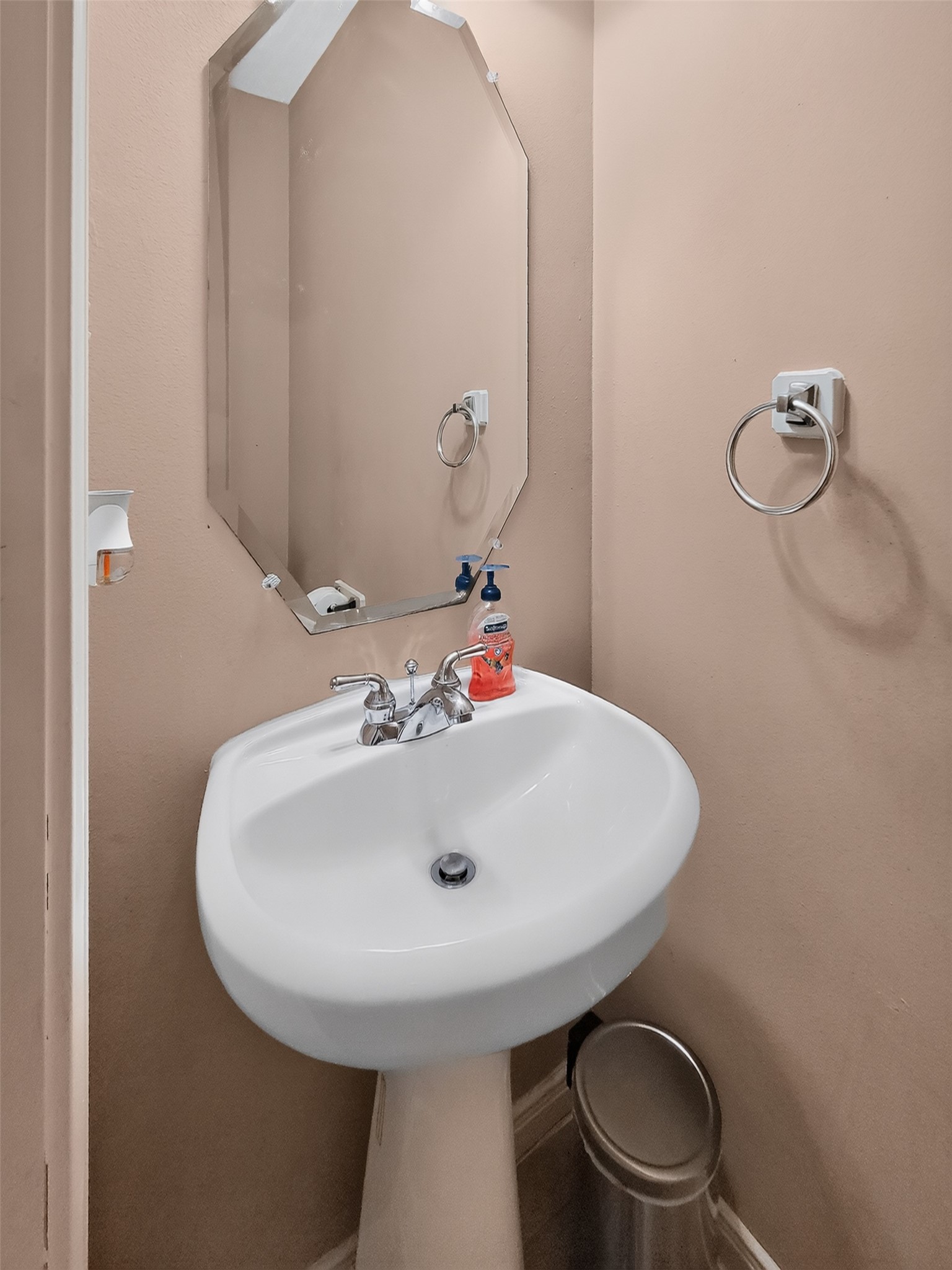 Charming half-bath with a sleek pedestal sink and modern octagonal mirror, perfect for guests.