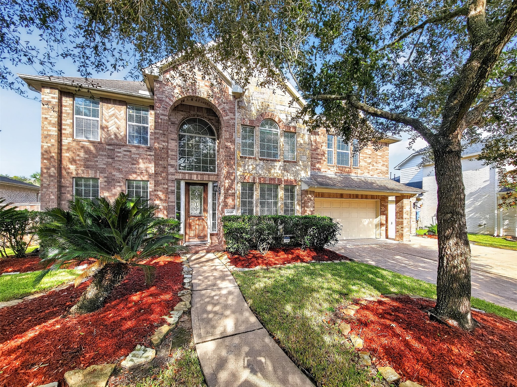 Stunning two-story brick home with elegant arched windows, a welcoming pathway, and lush landscaping, offering great curb appeal and a spacious two-car garage.