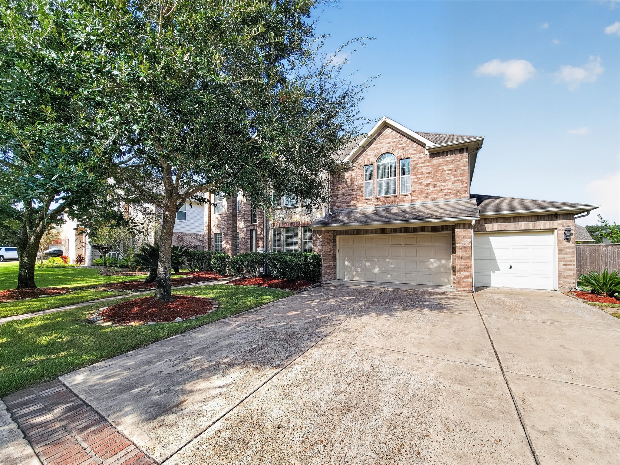 Stately two-story brick home with a spacious three-car garage, nestled among mature trees and lush landscaping.