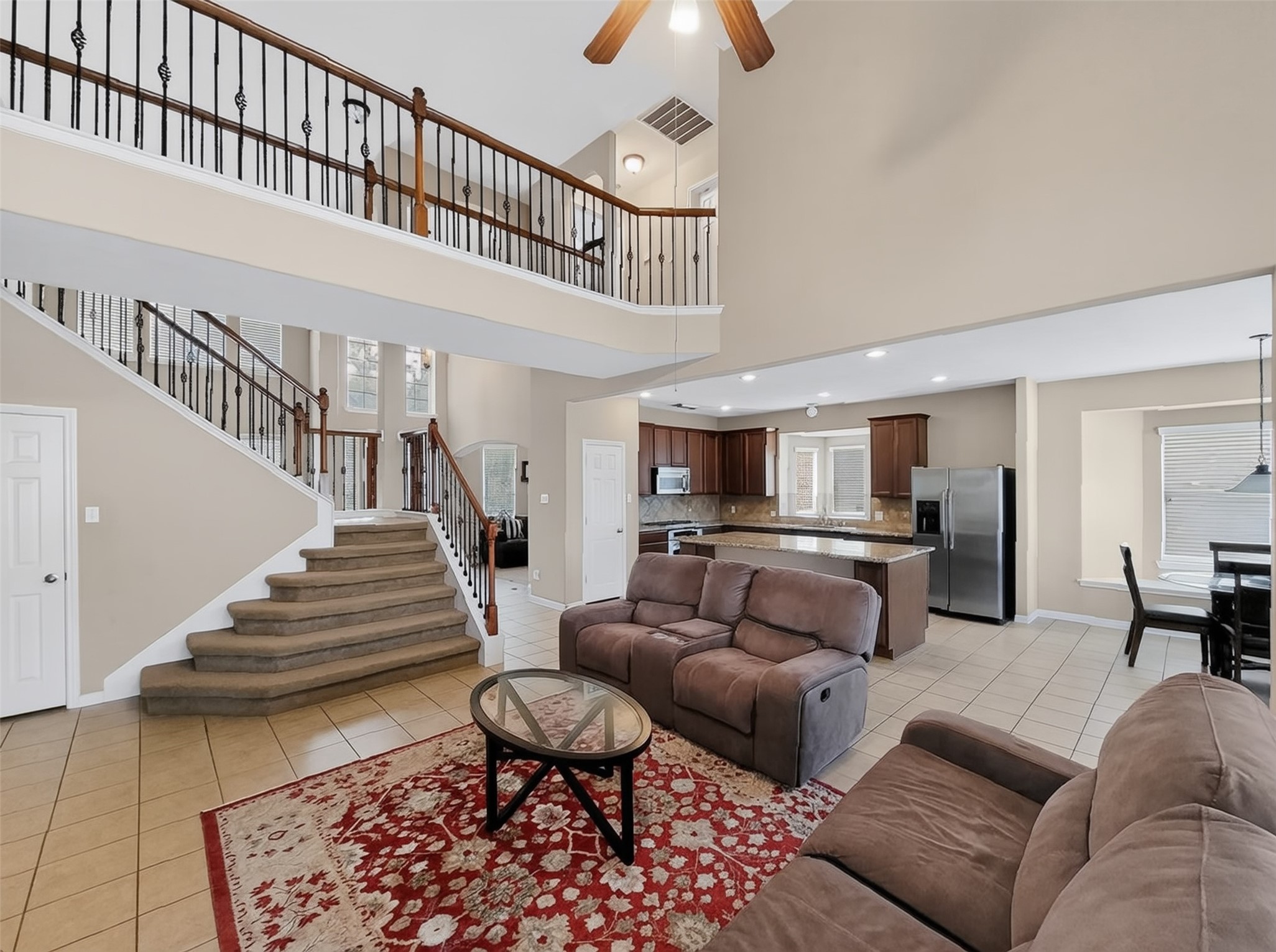 Spacious open-concept living area featuring a cozy seating arrangement, elegant staircase with wrought-iron railing, and a modern kitchen with stainless steel appliances and a central island.