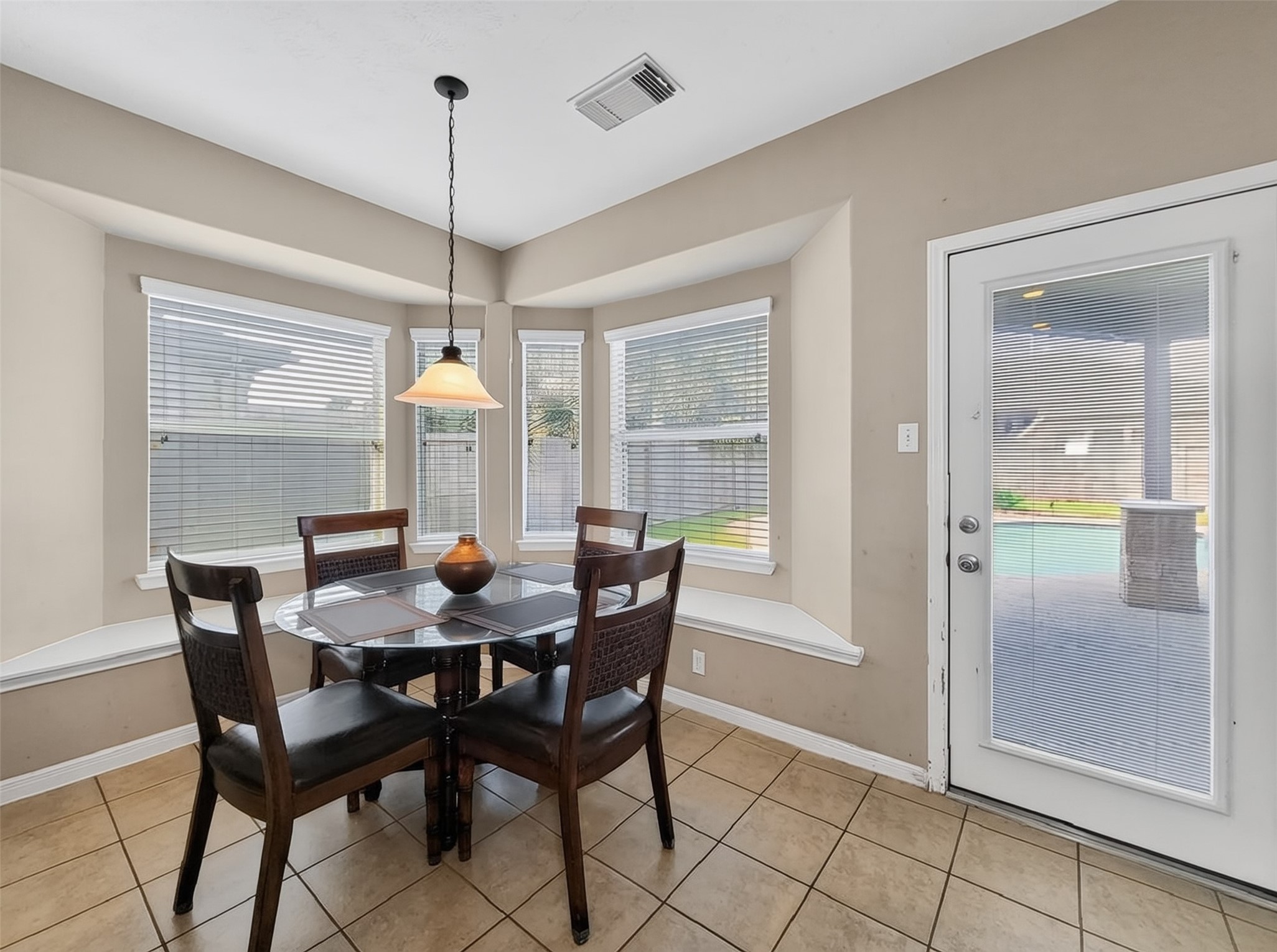 Bright breakfast nook with large bay windows, tile flooring, and a door leading to the backyard, perfect for enjoying morning light and easy outdoor access.