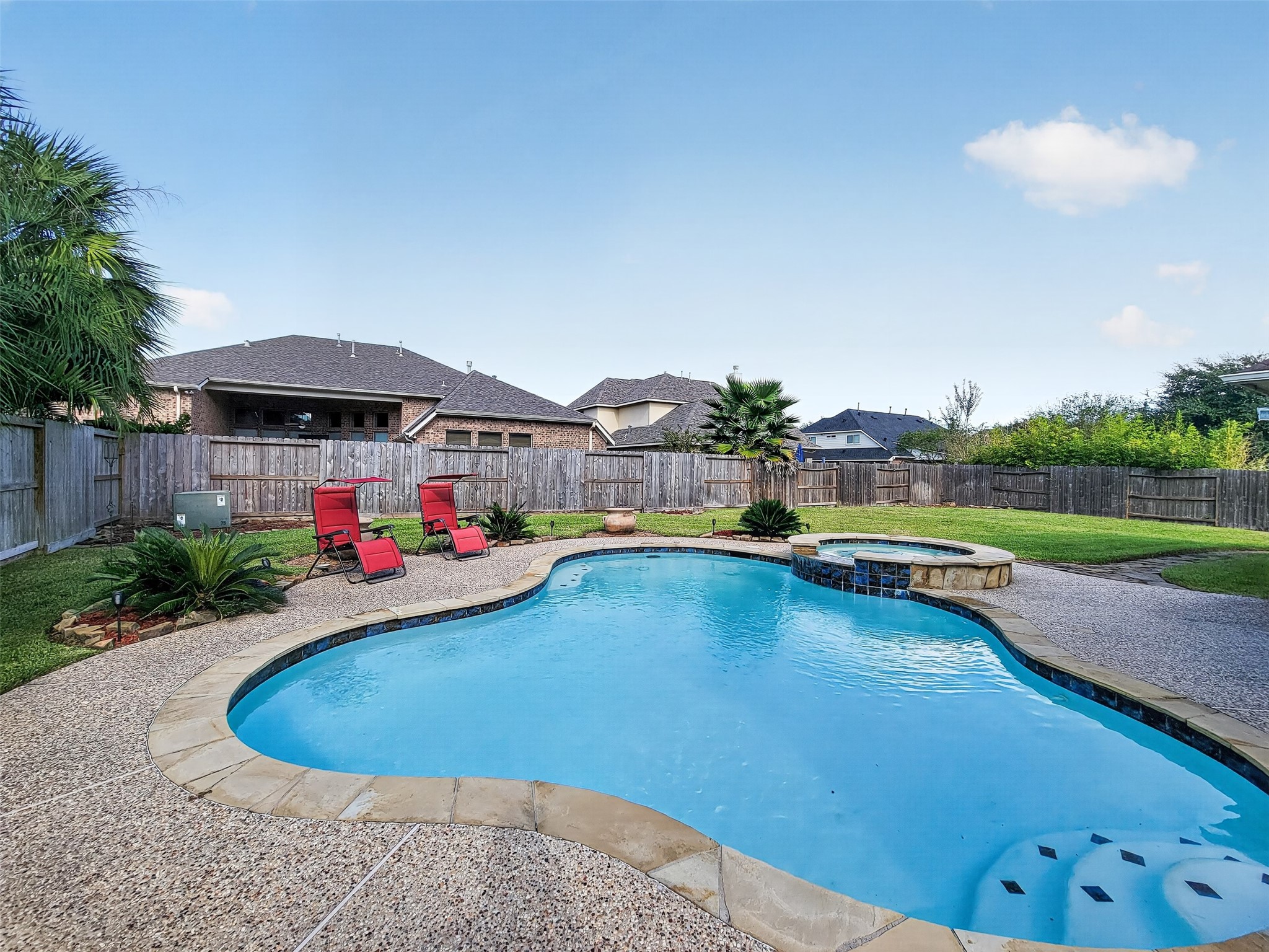 Charming backyard oasis featuring a sparkling pool with a spa, surrounded by a spacious patio and lush landscaping, perfect for relaxation and entertaining.