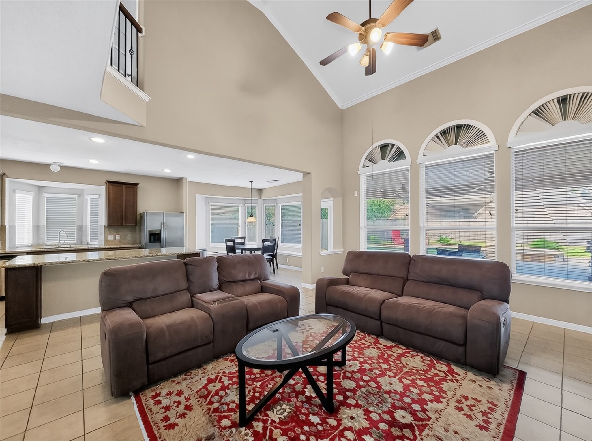 Spacious living area with high ceilings, featuring large arched windows for ample natural light, an open layout connecting to a modern kitchen with granite countertops, and a cozy seating arrangement on a stylish red rug.
