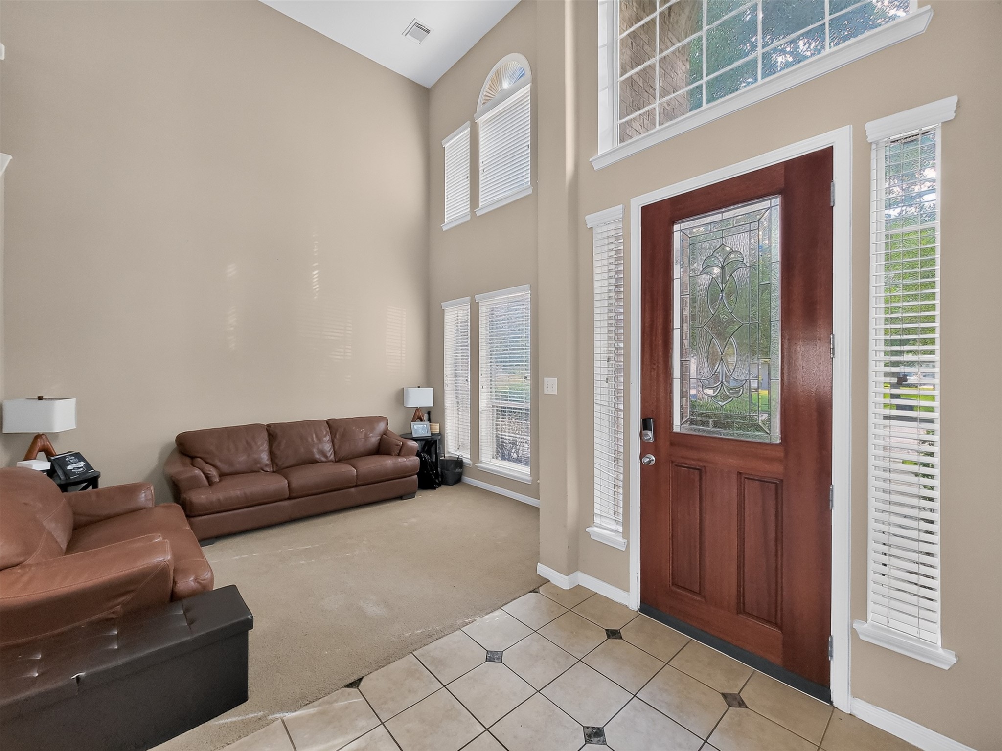 Grand entrance featuring a beautifully crafted wooden door with intricate glass design, leading into a spacious living area with high ceilings and abundant natural light.
