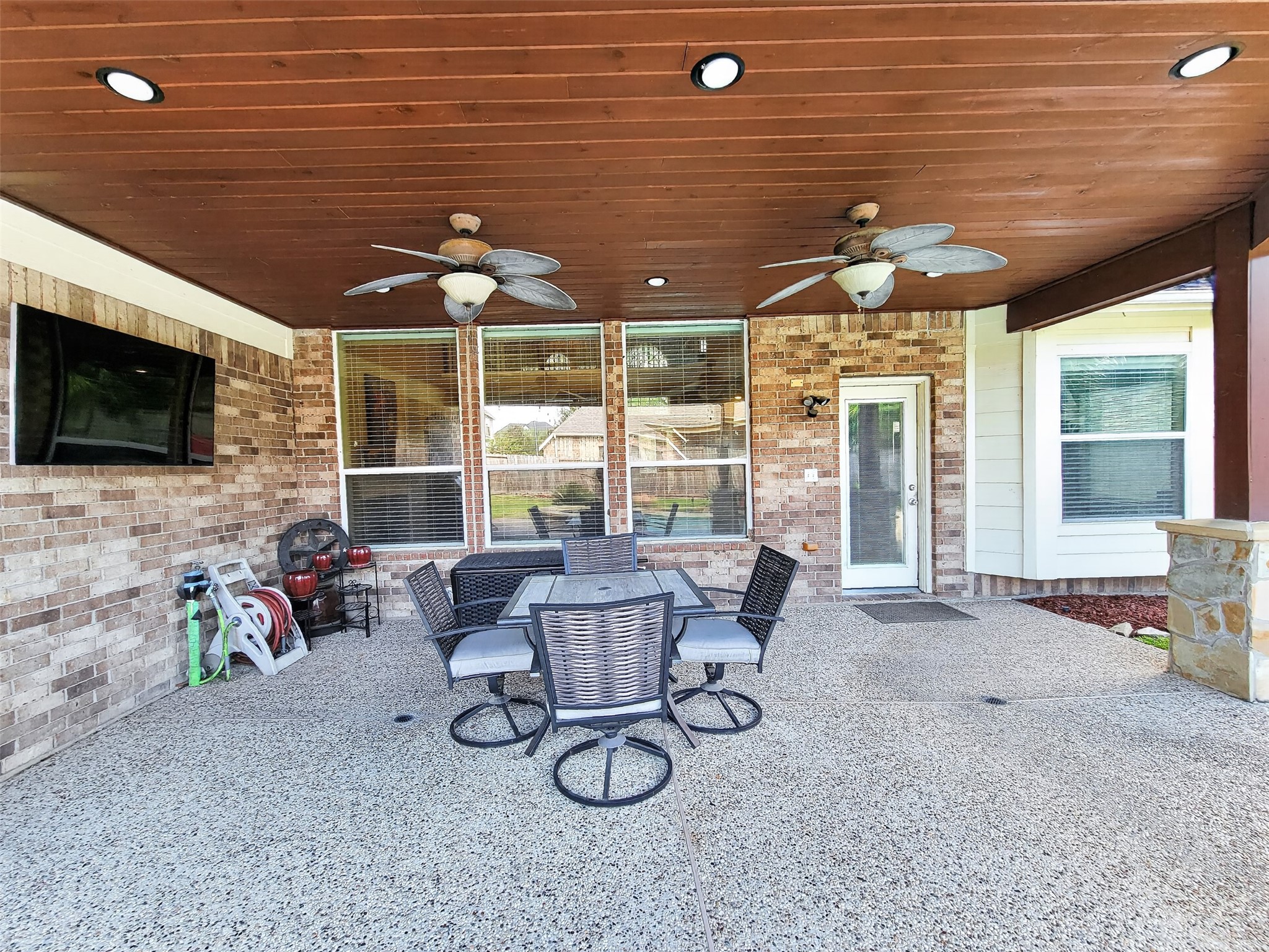 Spacious covered patio featuring a ceiling with recessed lighting and fans, perfect for outdoor dining and entertainment, complete with a mounted TV for relaxation.