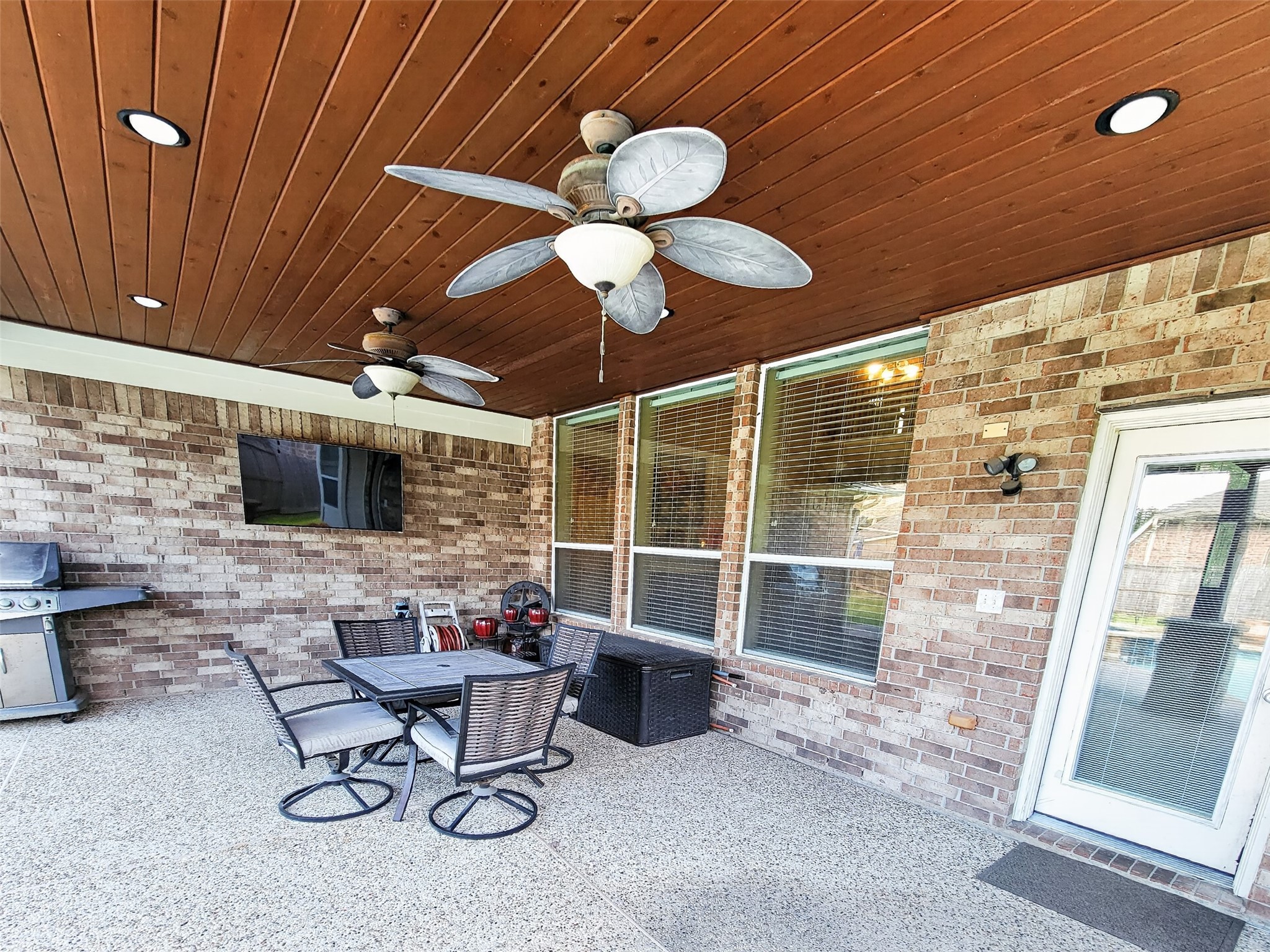 Spacious covered patio featuring a wood-paneled ceiling with fans, perfect for outdoor entertaining, complete with a dining area, grill, and mounted TV.